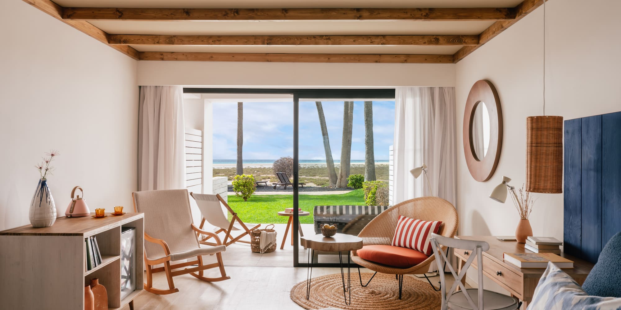 Interior de habitación costera con vista al mar, palmeras y patio.