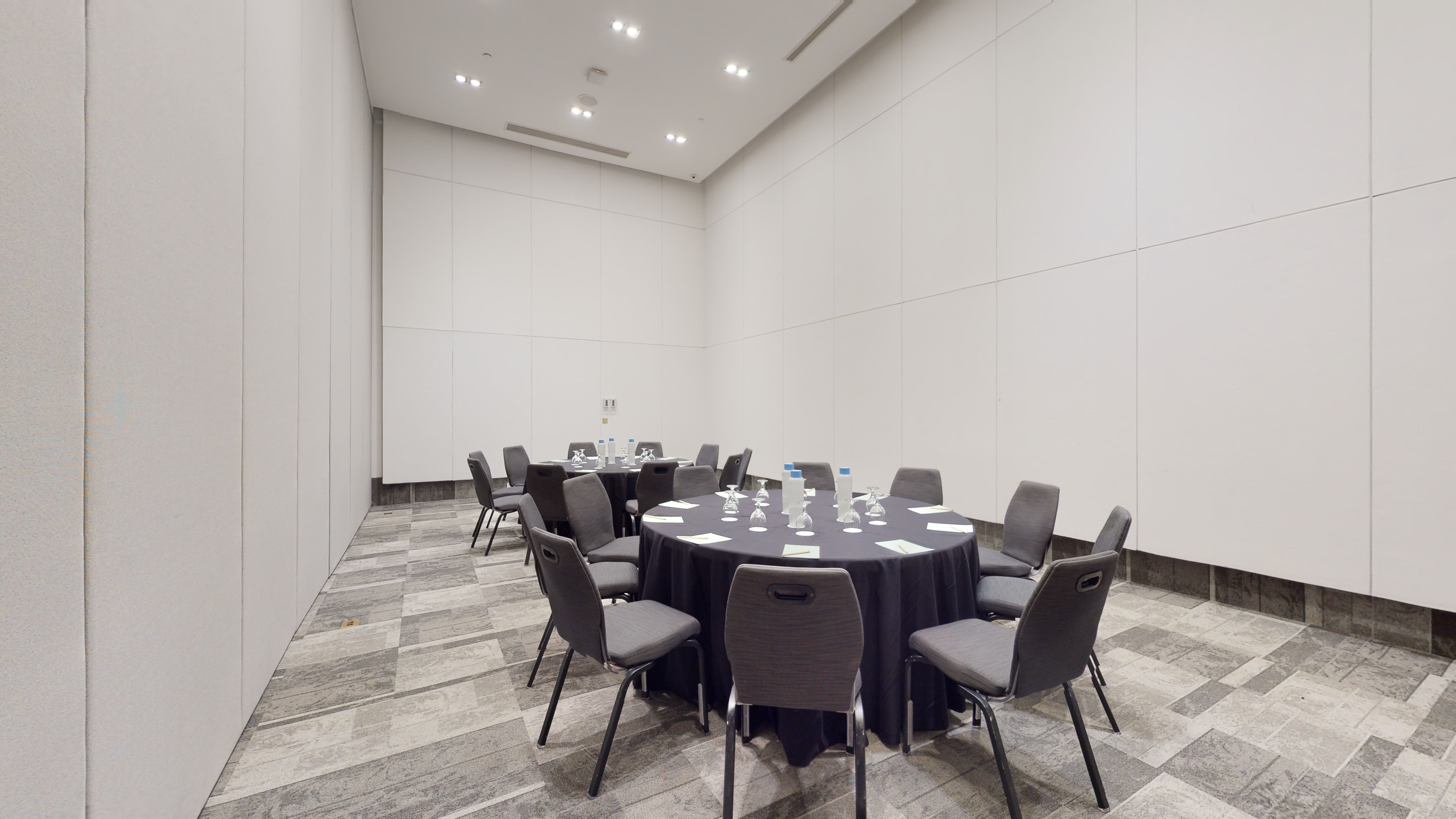 Modern meeting room with round tables, grey chairs, and white panel walls.