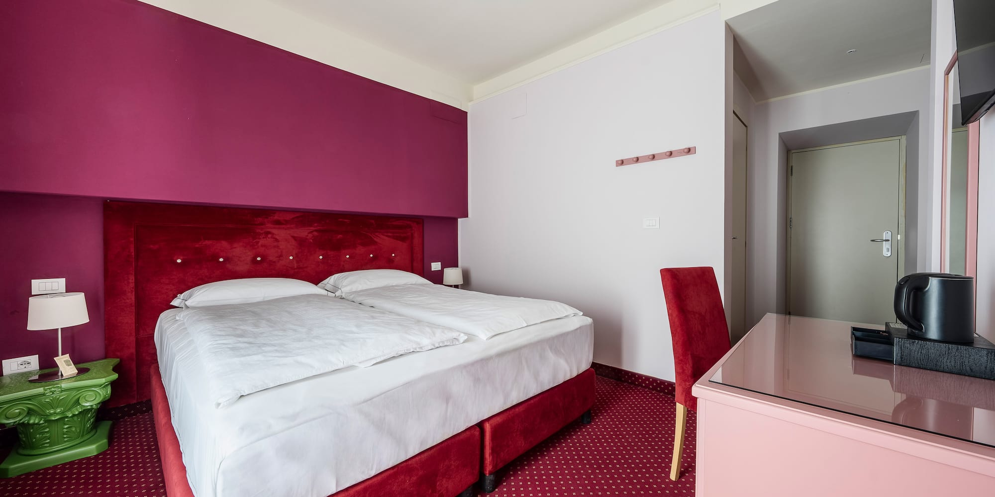 Hotel room with red velvet bed, magenta wall, and patterned red carpet.