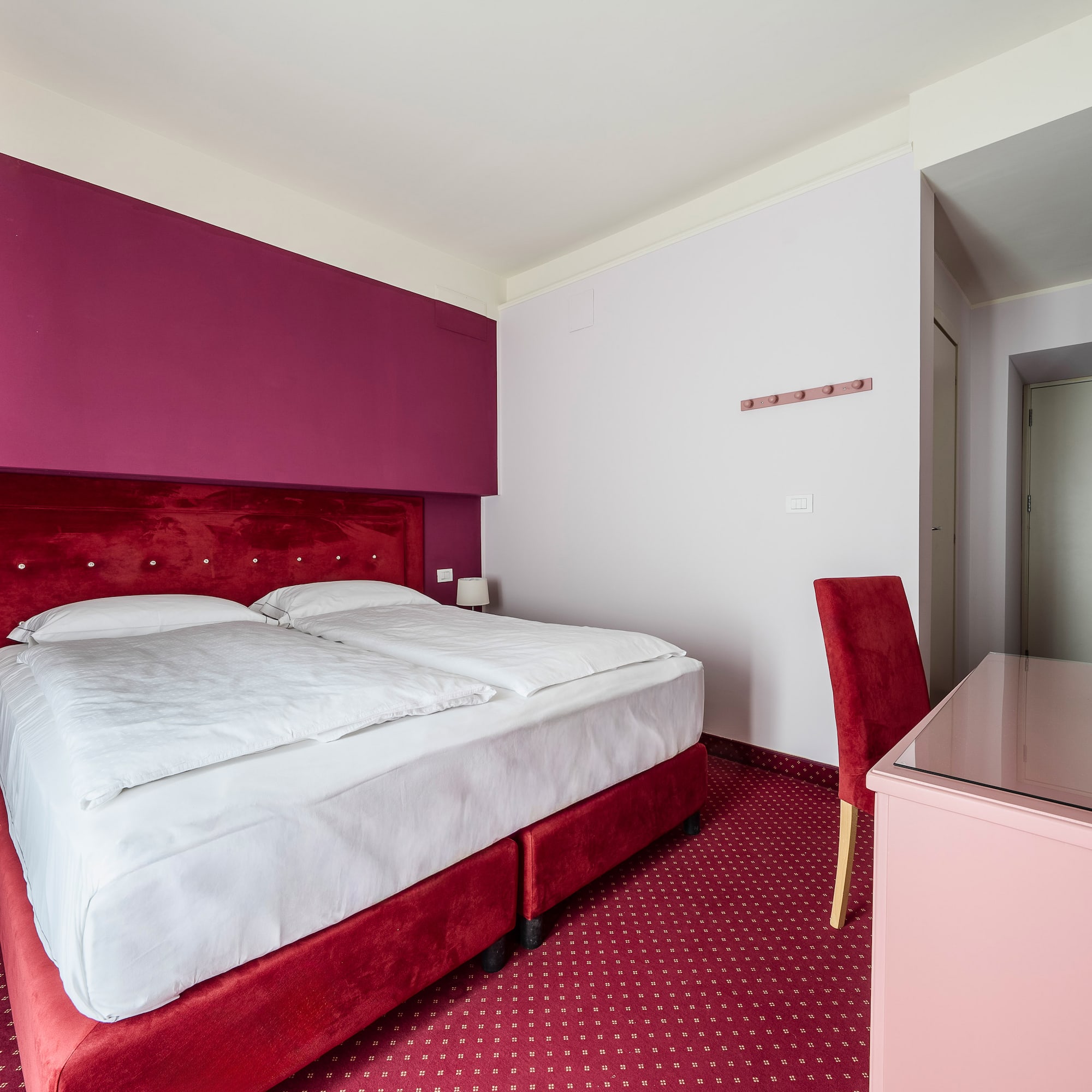 Hotel room with red velvet bed, magenta wall, and patterned red carpet.
