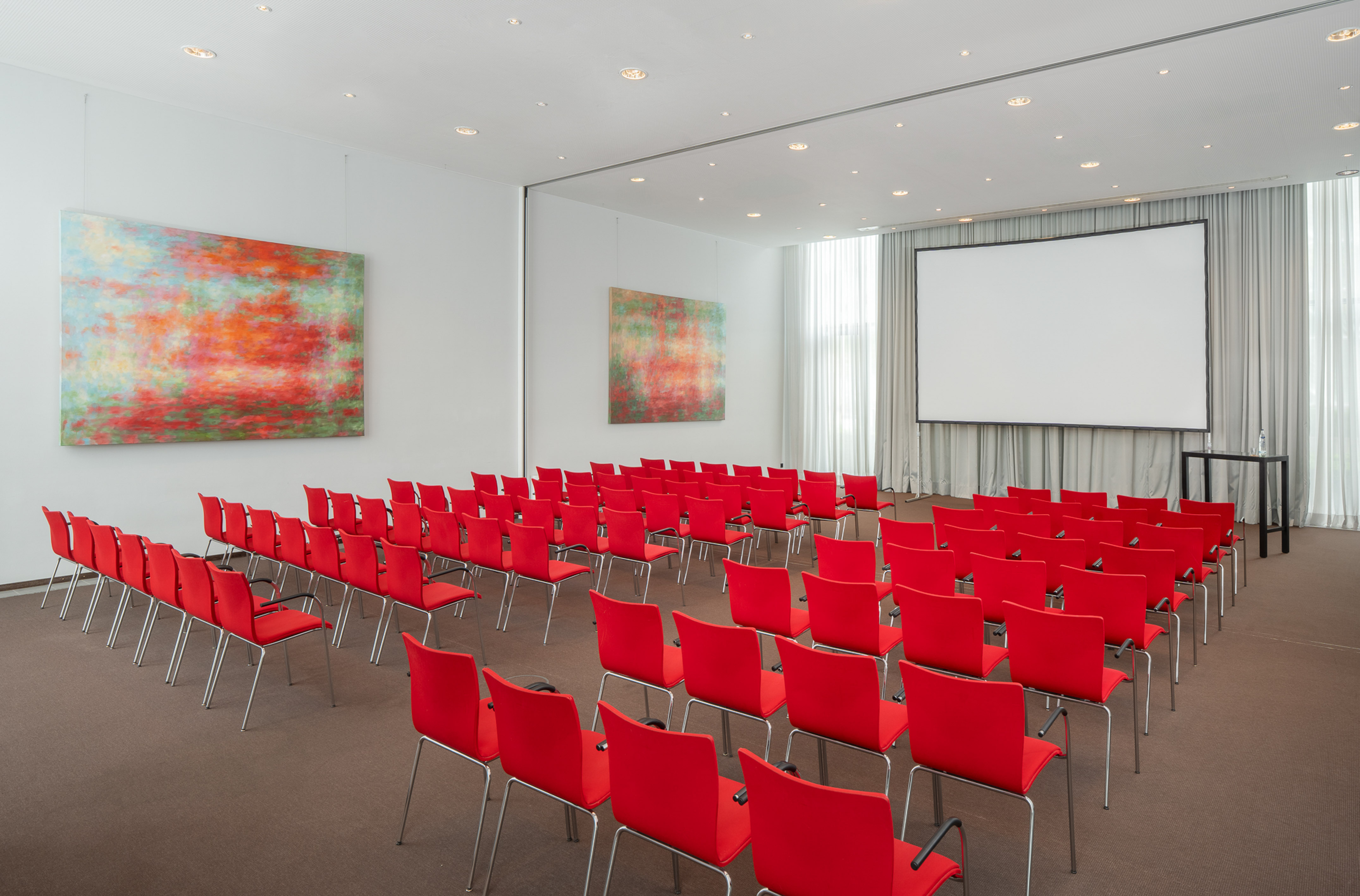 Modern conference room with red chairs, projector screen, and abstract art.