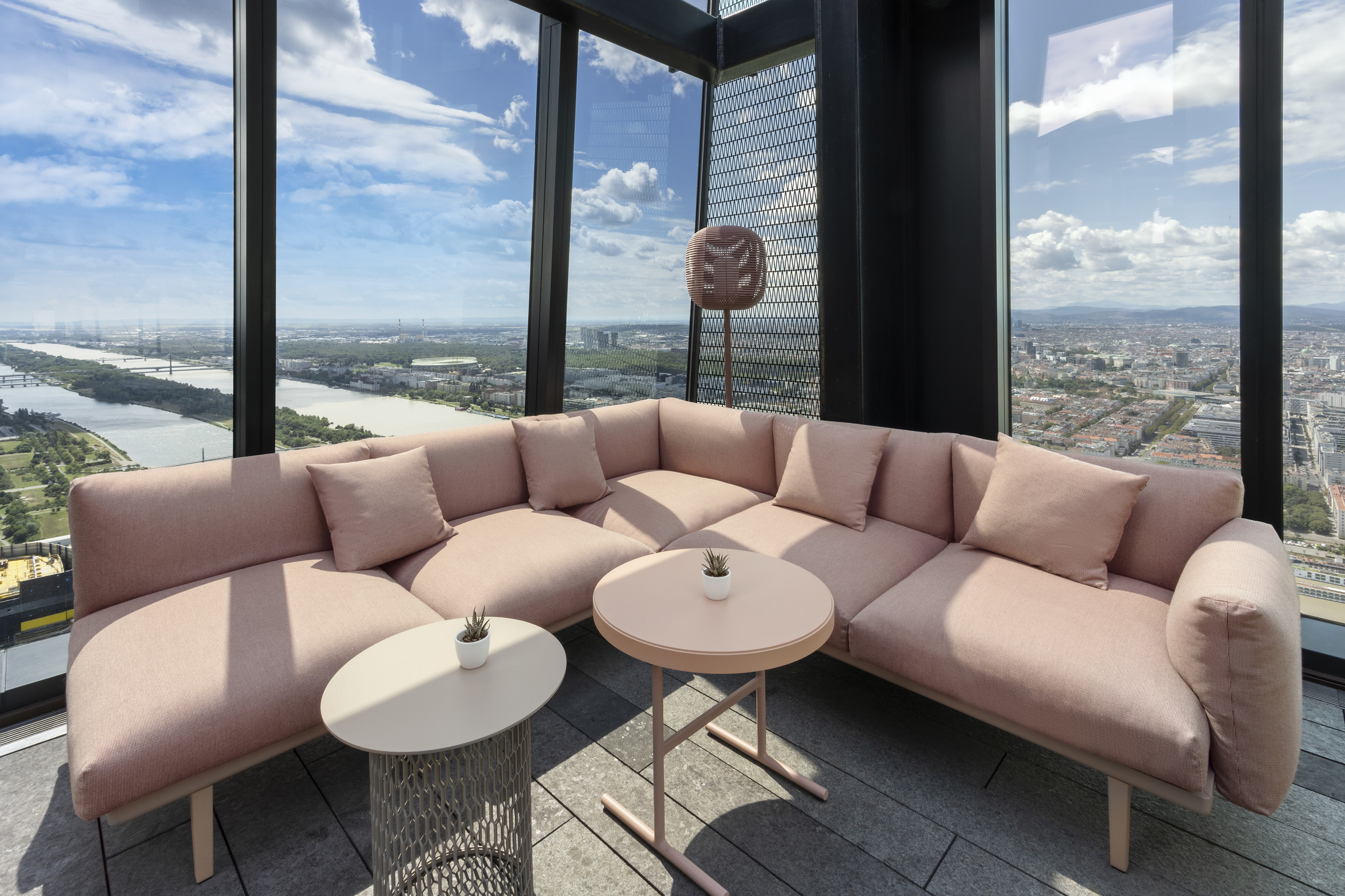Modern rooftop lounge with pink sectional sofa and panoramic city view.