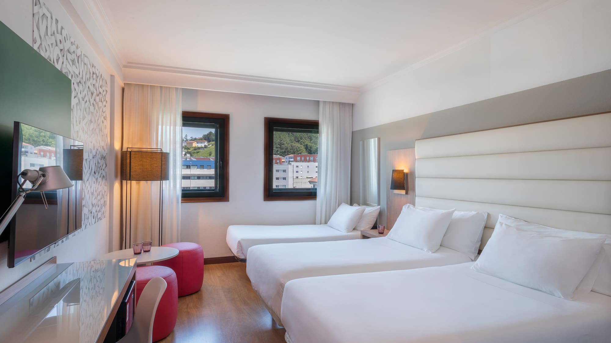 Triple hotel room with three single beds, desk, and two windows.