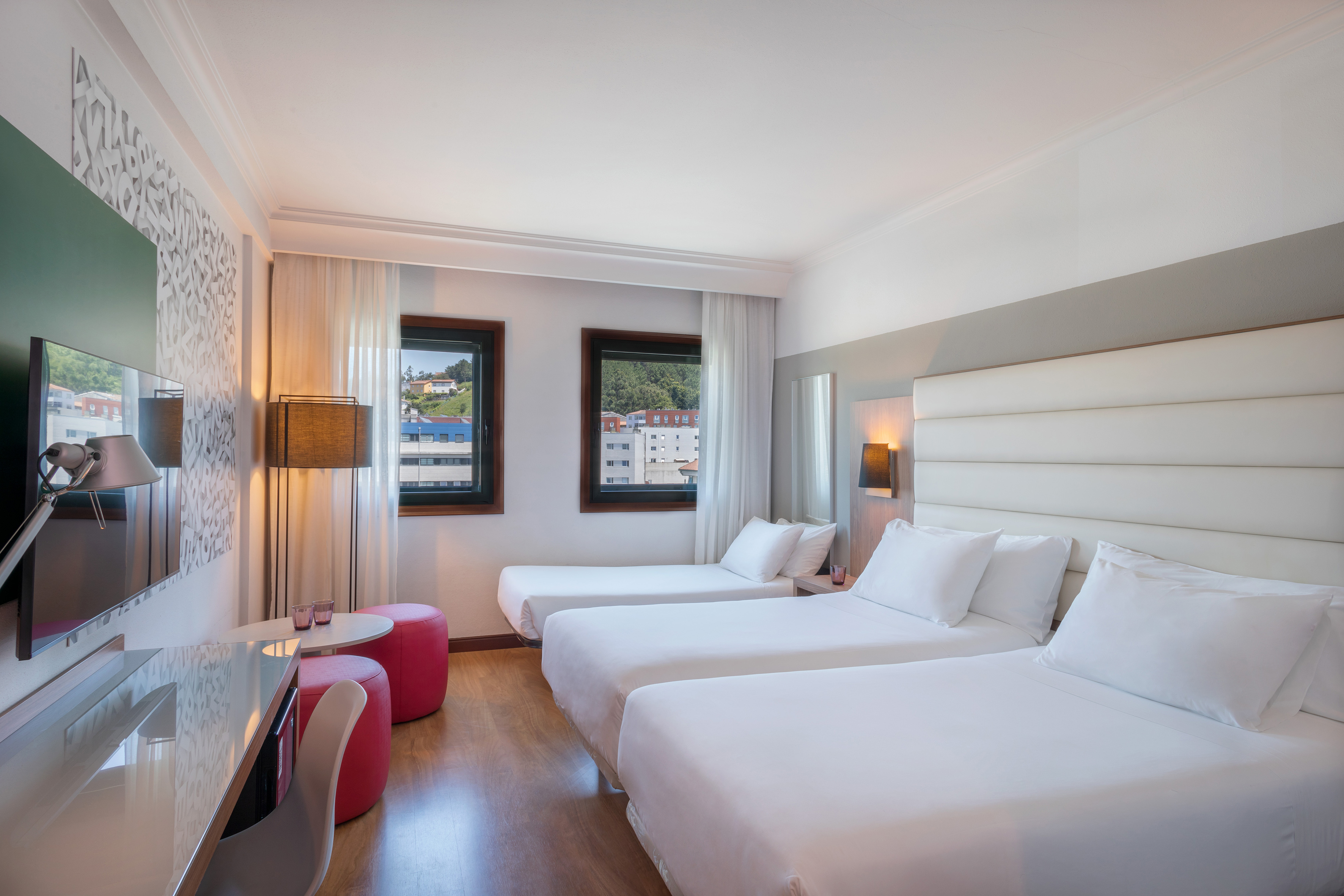 Triple hotel room with three single beds, desk, and two windows.