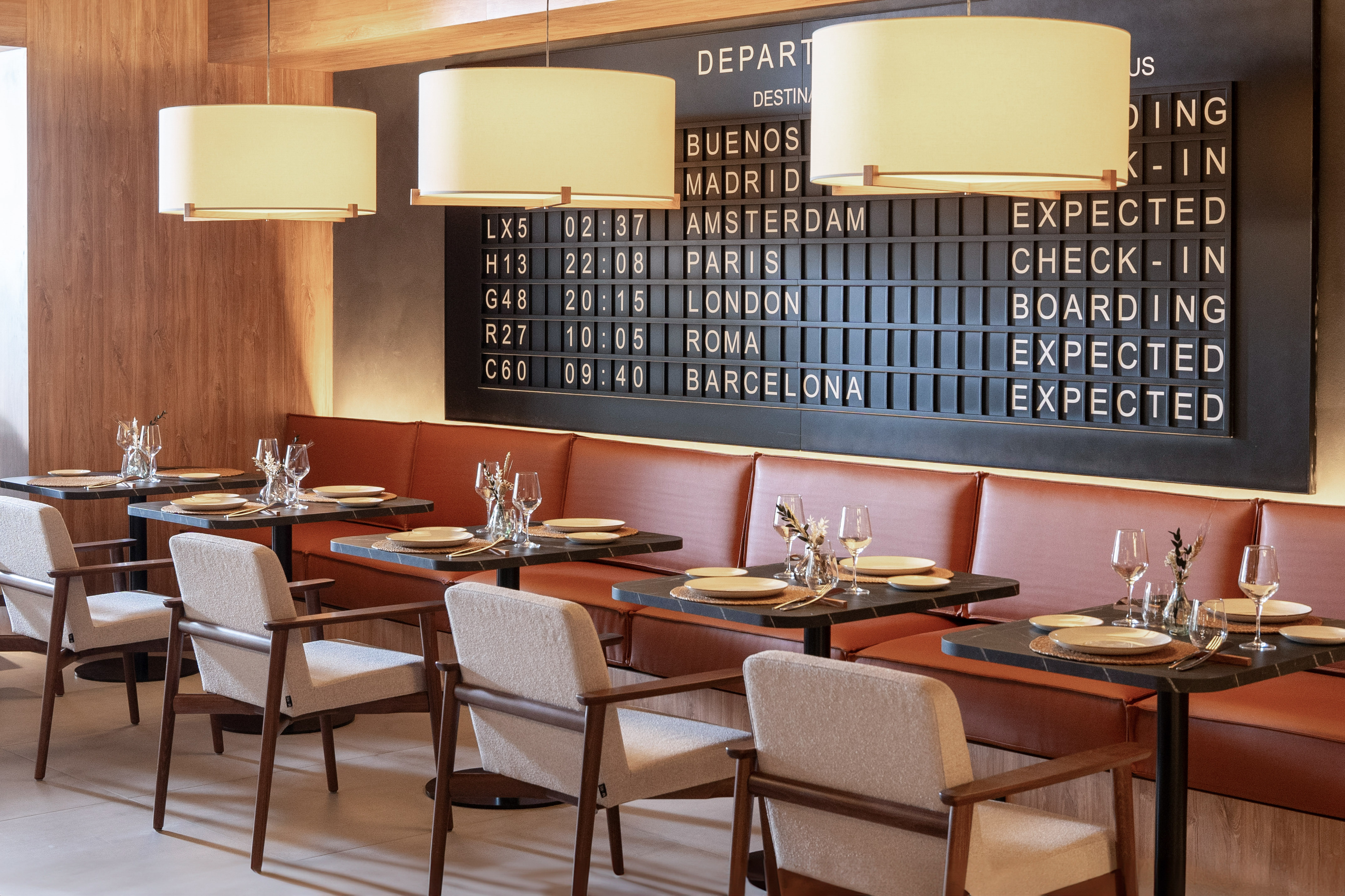Modern restaurant with airport departure board, dining tables, and booth seating.