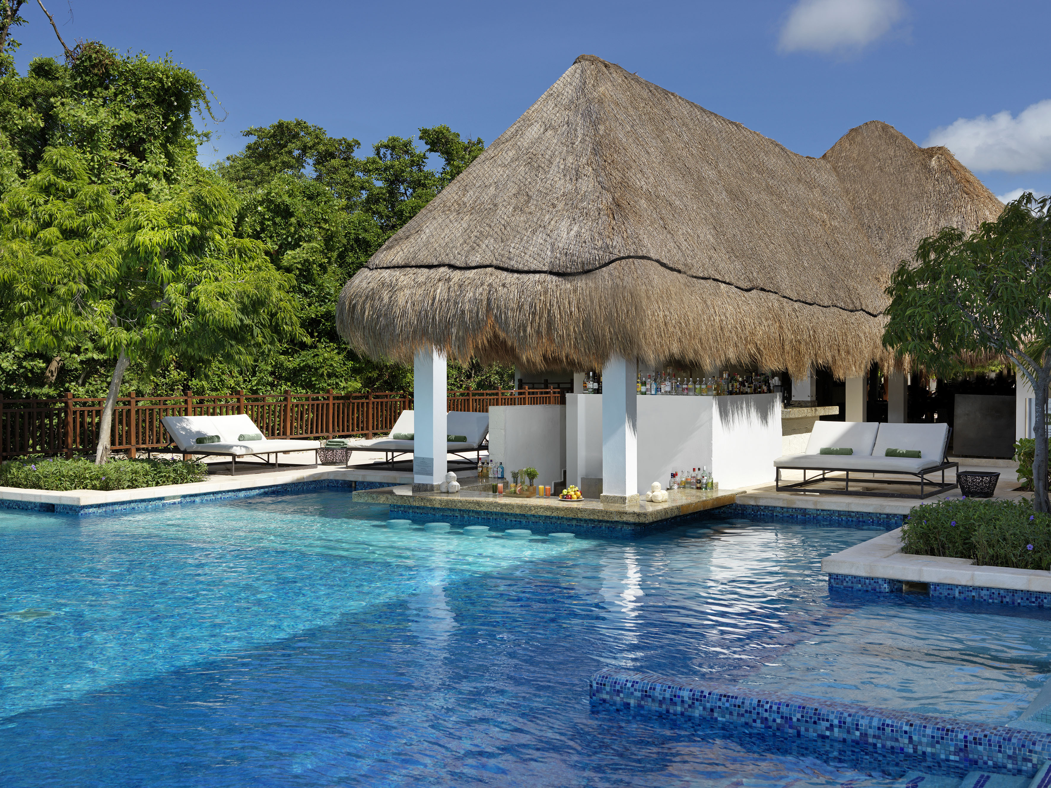 Vibrant resort pool with thatched swim-up bar, green trees.