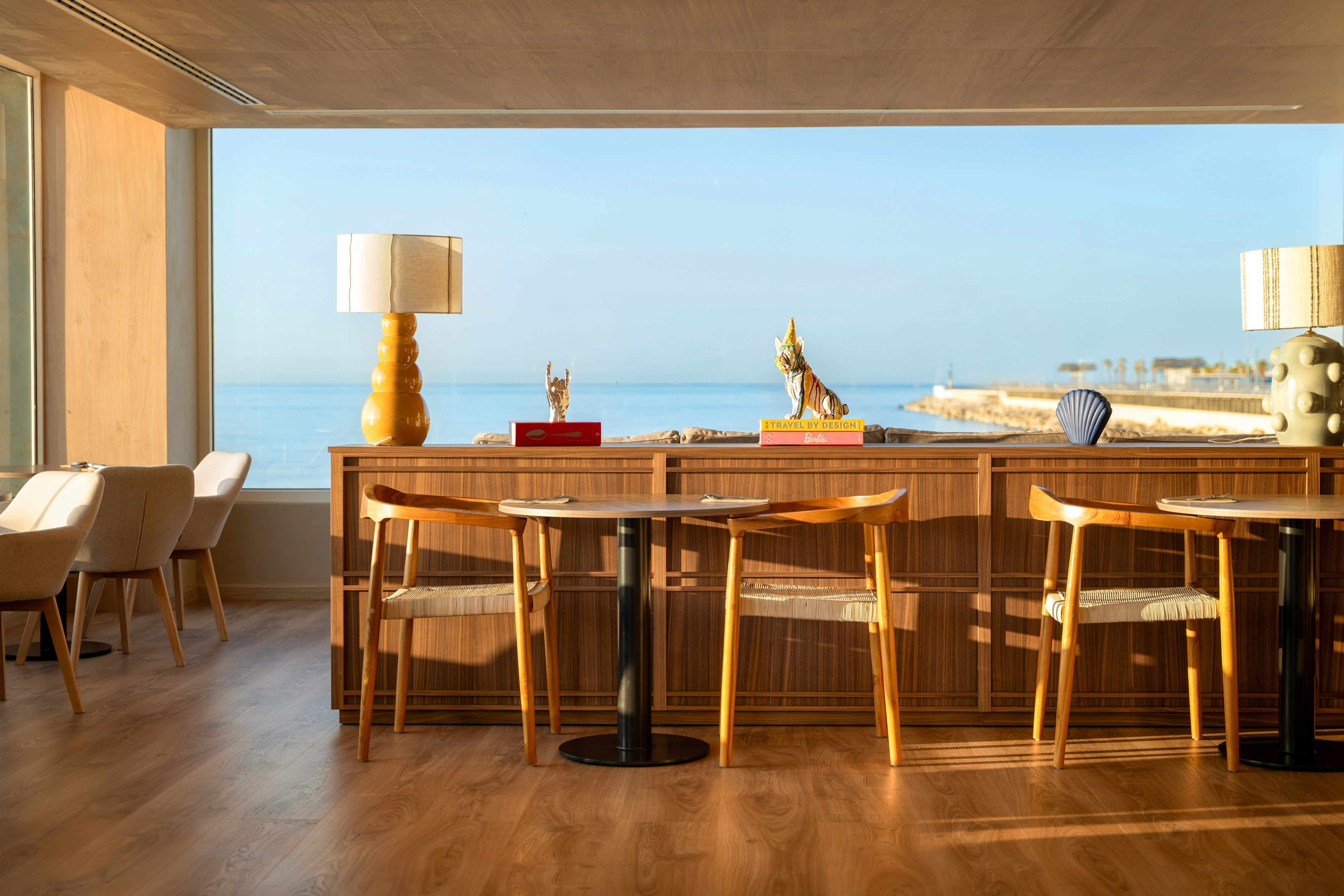 Bright modern restaurant interior with ocean view and wooden decor.