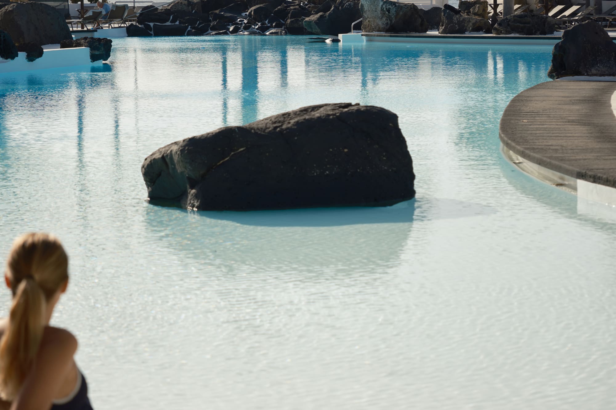 Woman relaxing by a tropical pool with palm trees and distant ocean.