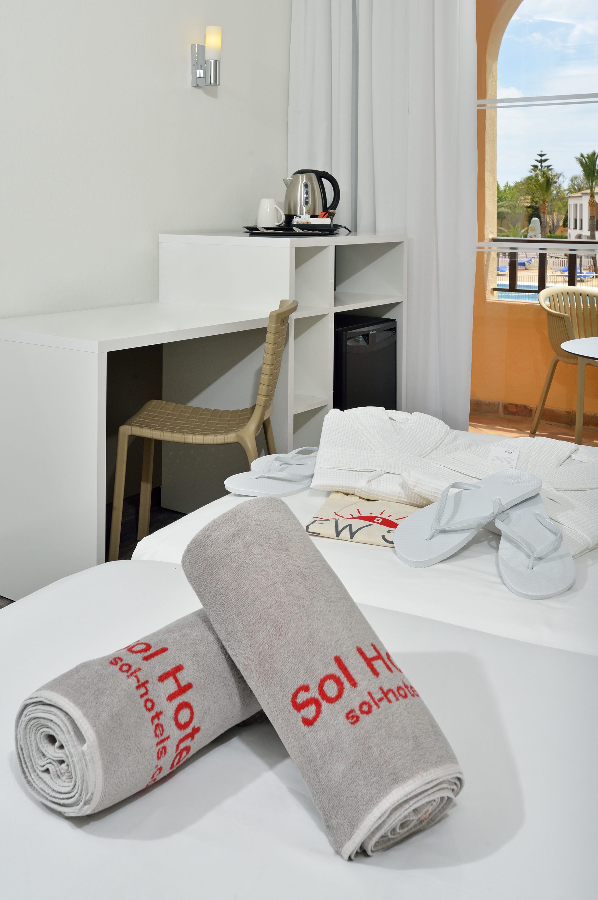 Hotel room with Sol Hotels towels, bathrobes, flip-flops, and balcony pool view.
