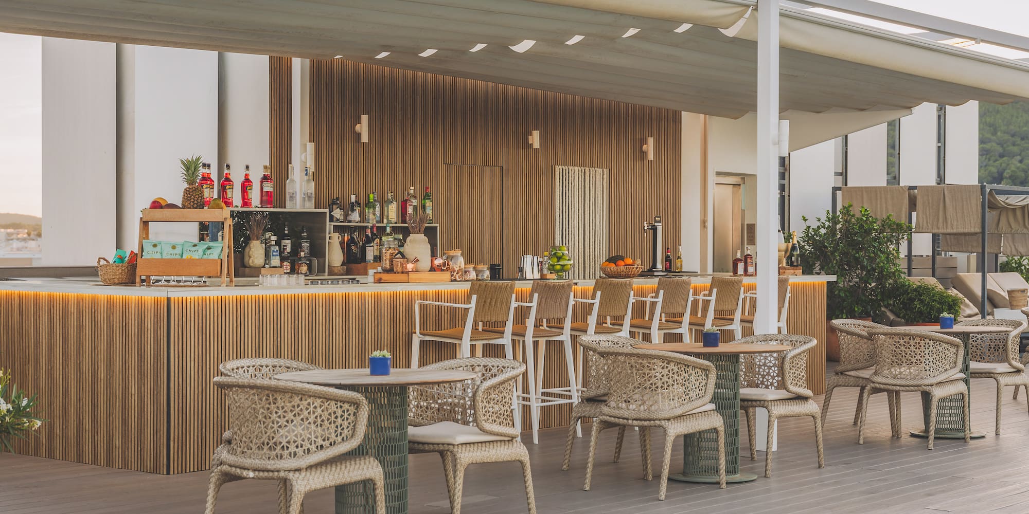 Modern outdoor hotel bar by pool with wooden counter and woven chairs.