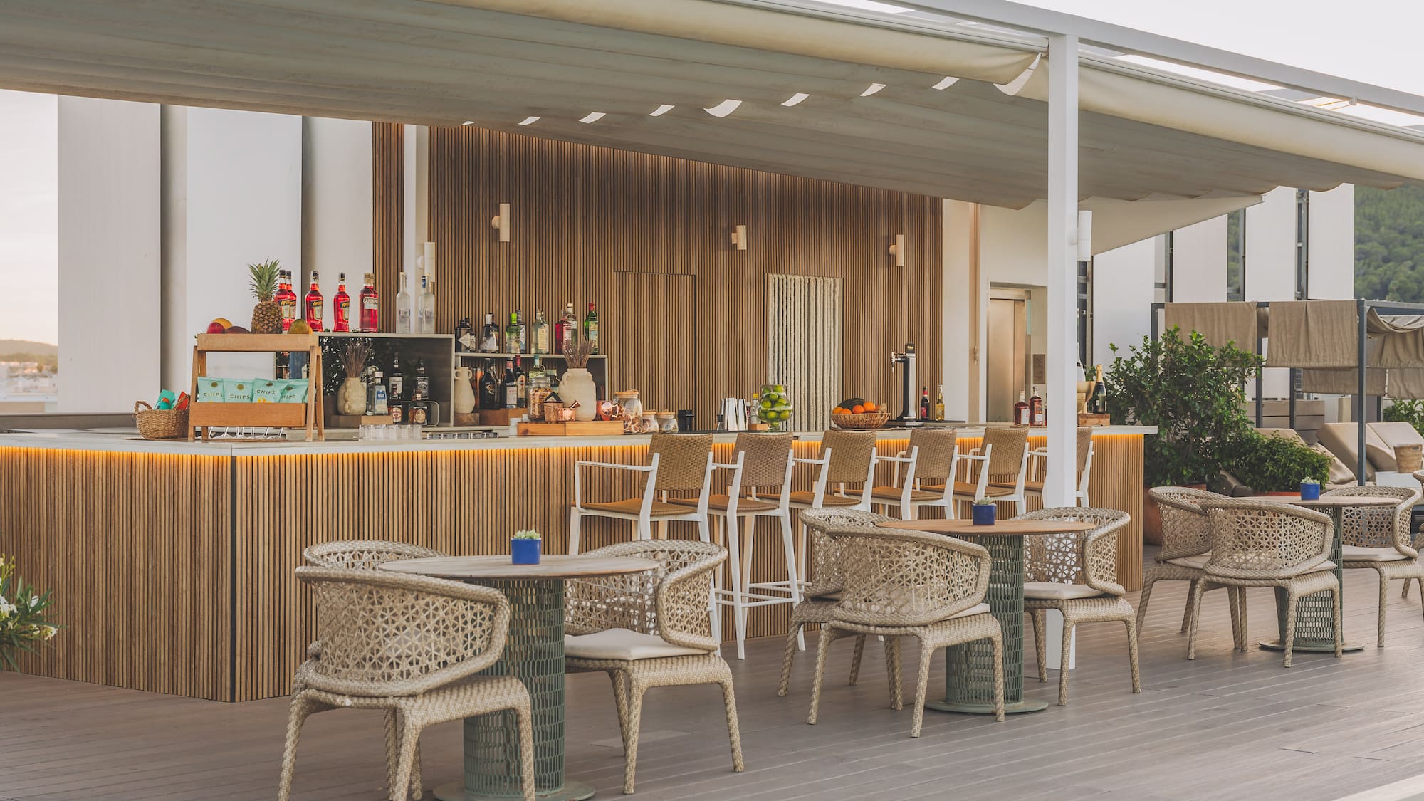 Modern outdoor hotel bar by pool with wooden counter and woven chairs.