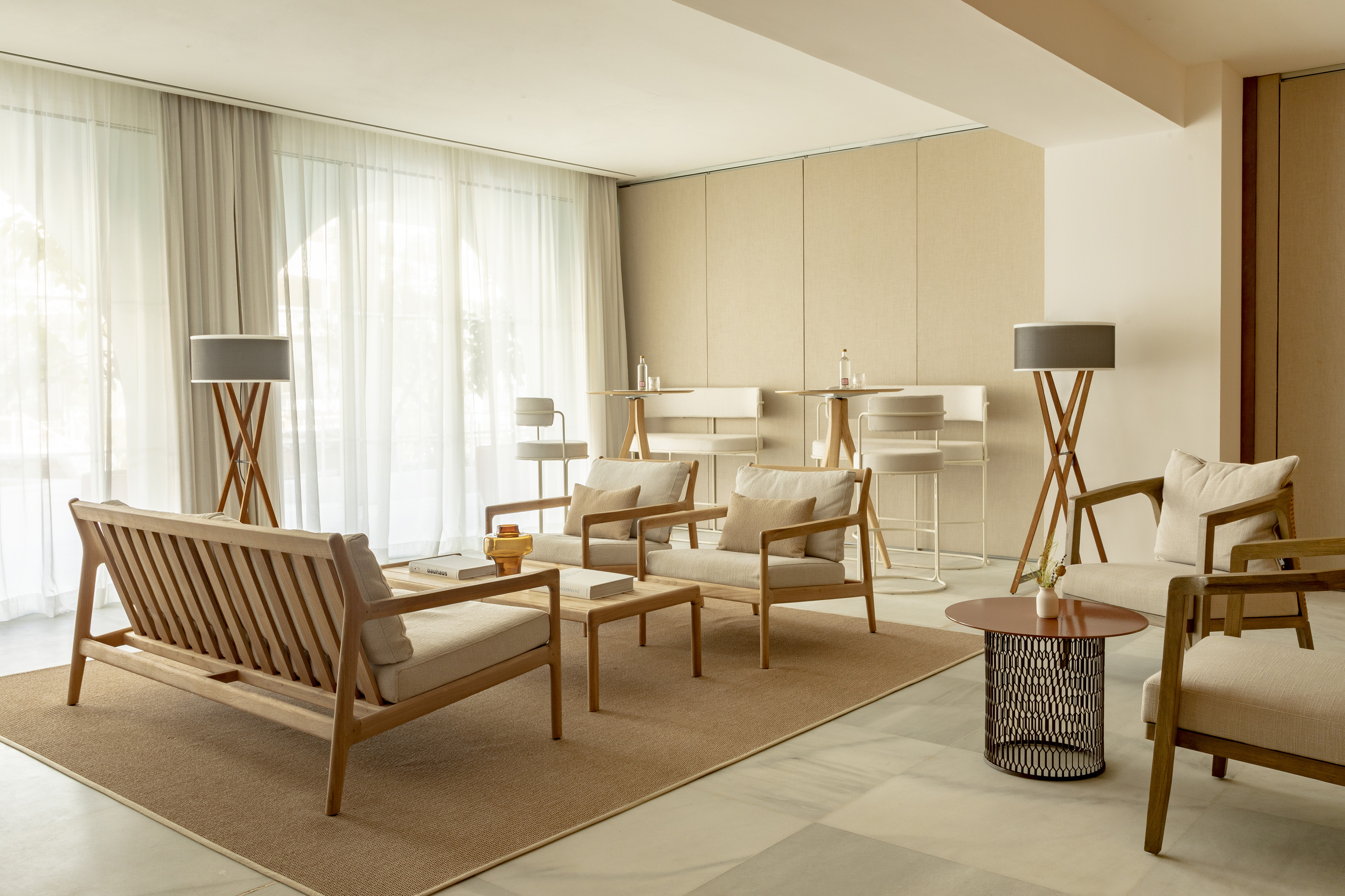 Modern lounge with wooden sofa, armchairs, coffee tables, and neutral decor.