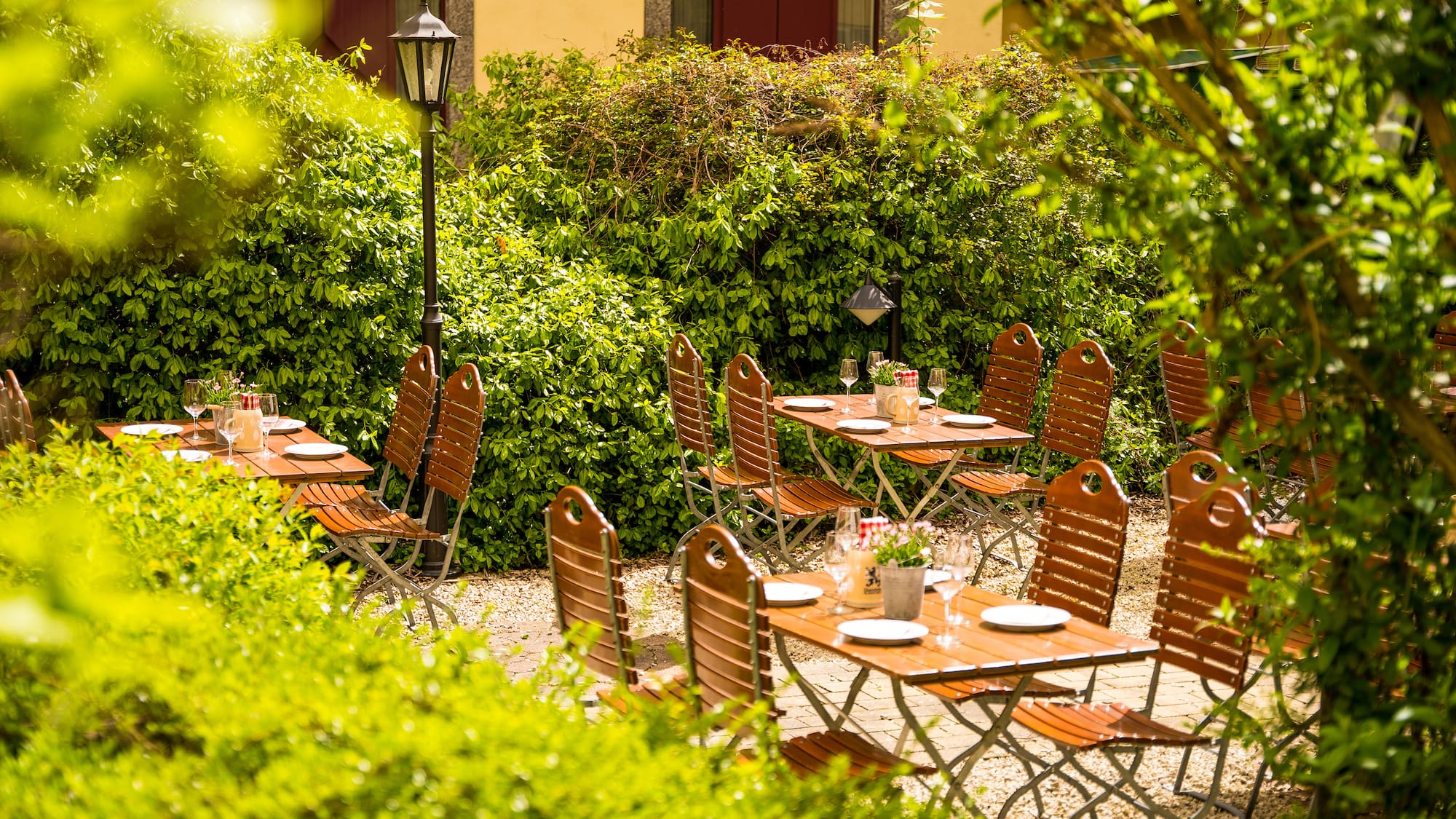 a table and chairs outside with bushes and a building