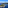 Helicopter flying above a green coastal island with yachts in a blue ocean.