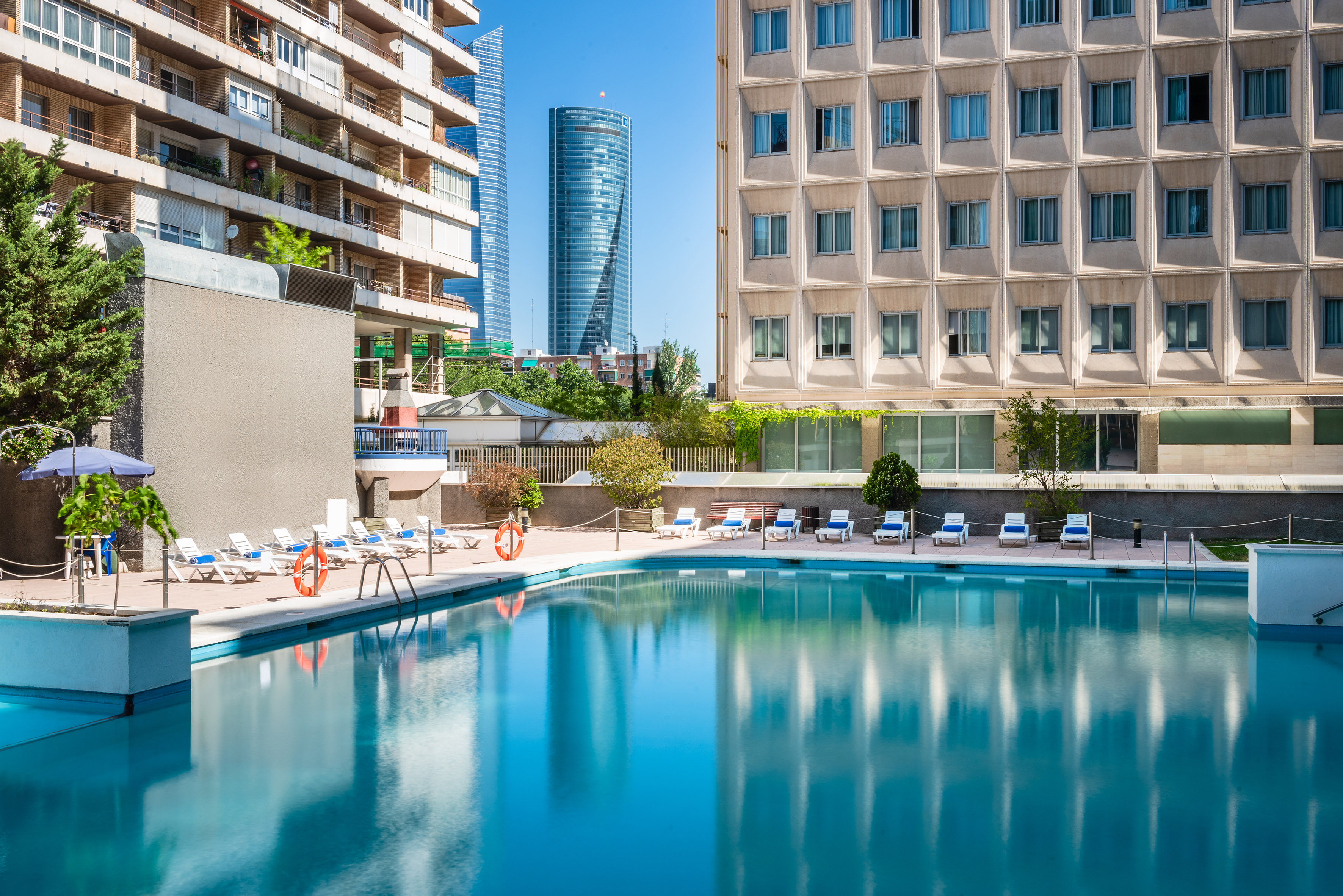 A pool surrounded by chairs, with a building in the background.