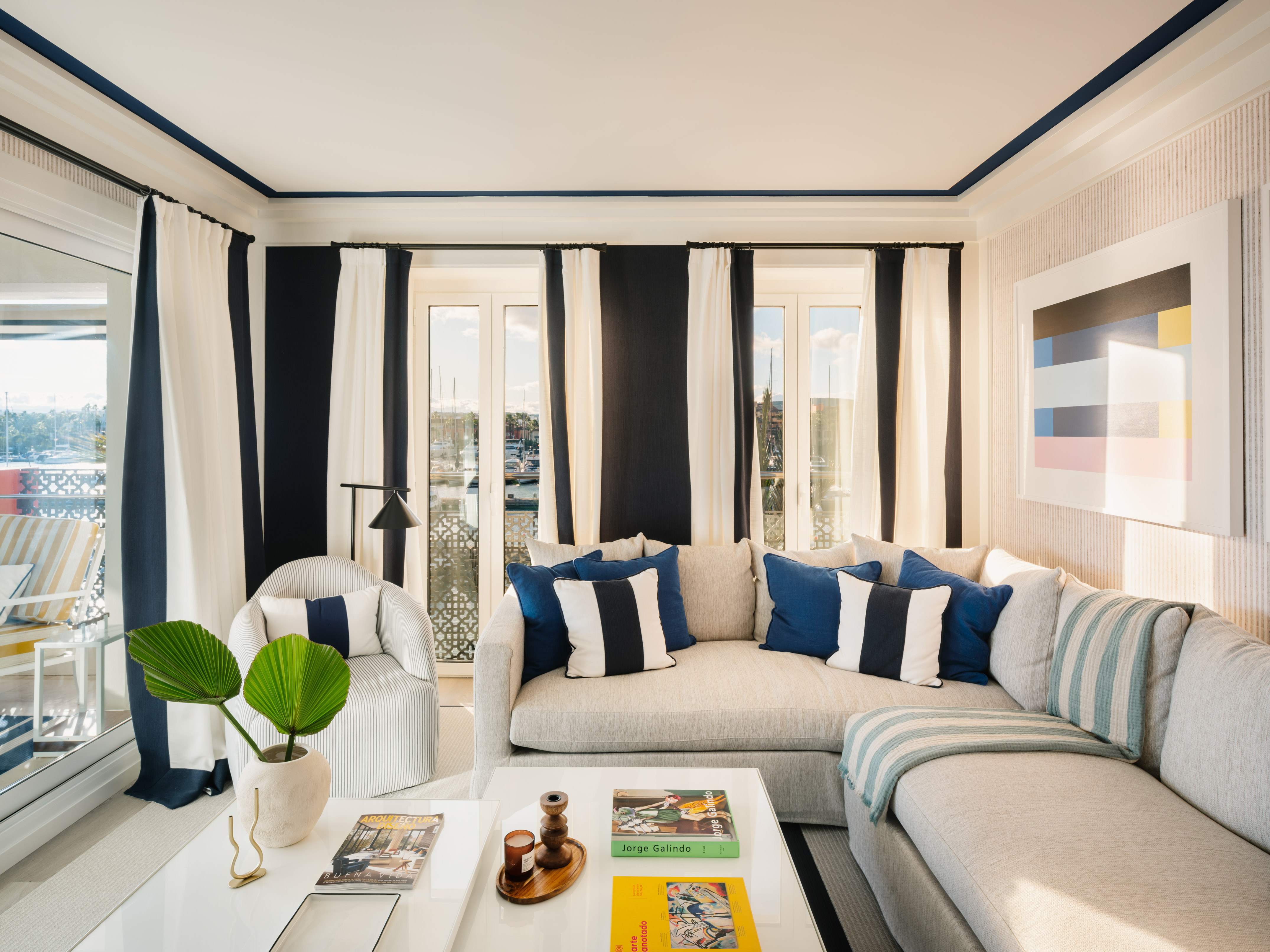 Coastal living room with navy and white stripes, grey sectional, and marina view.