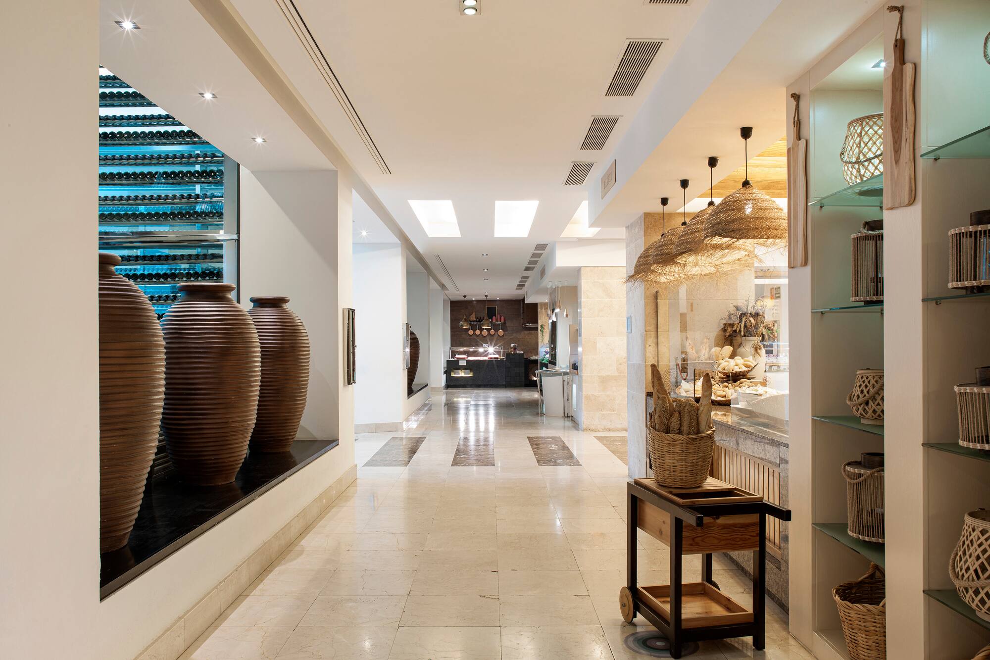 Modern hotel lobby with wine display, marble floors, and bakery buffet.