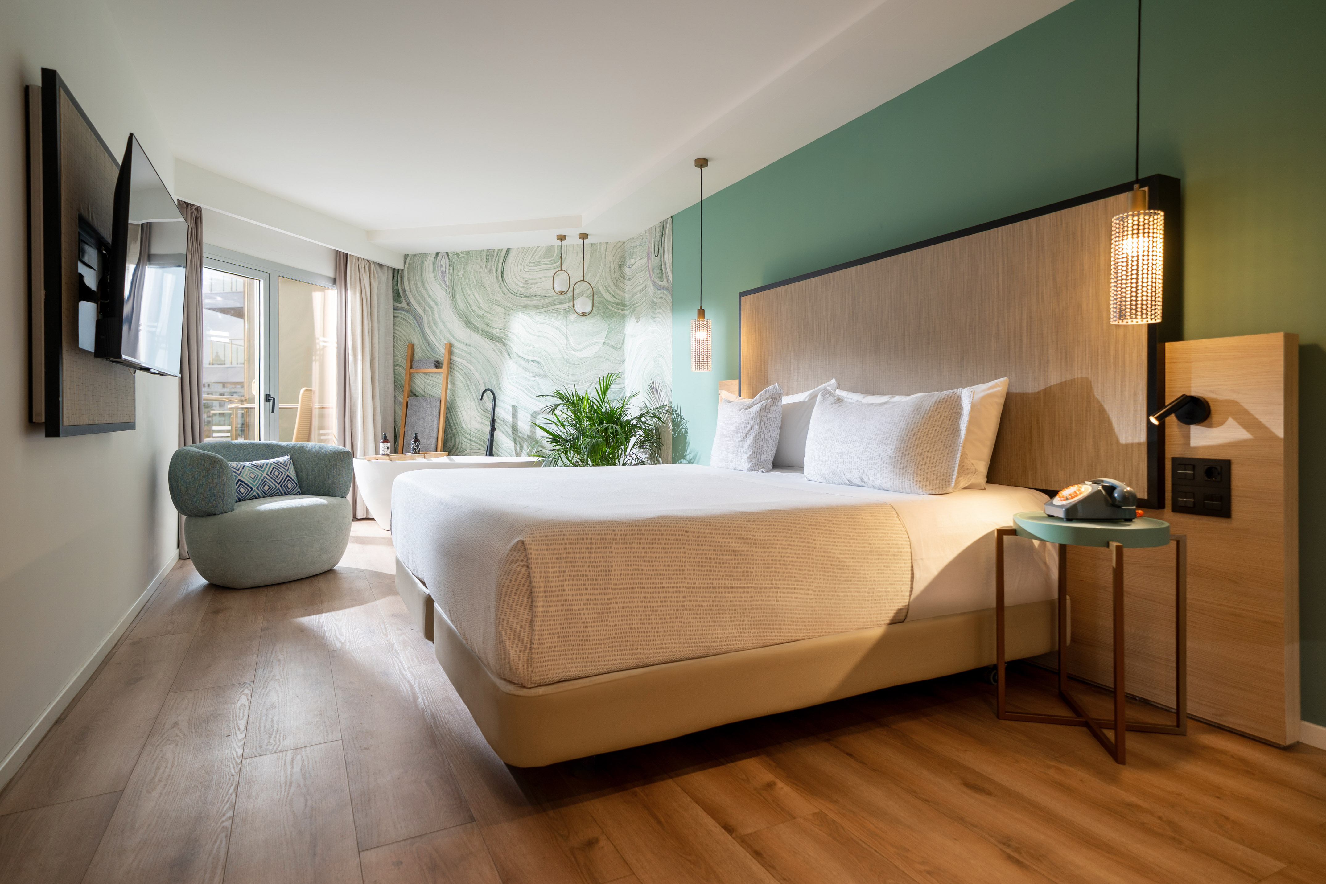 Modern hotel room, large bed, green accent wall, freestanding tub, balcony.