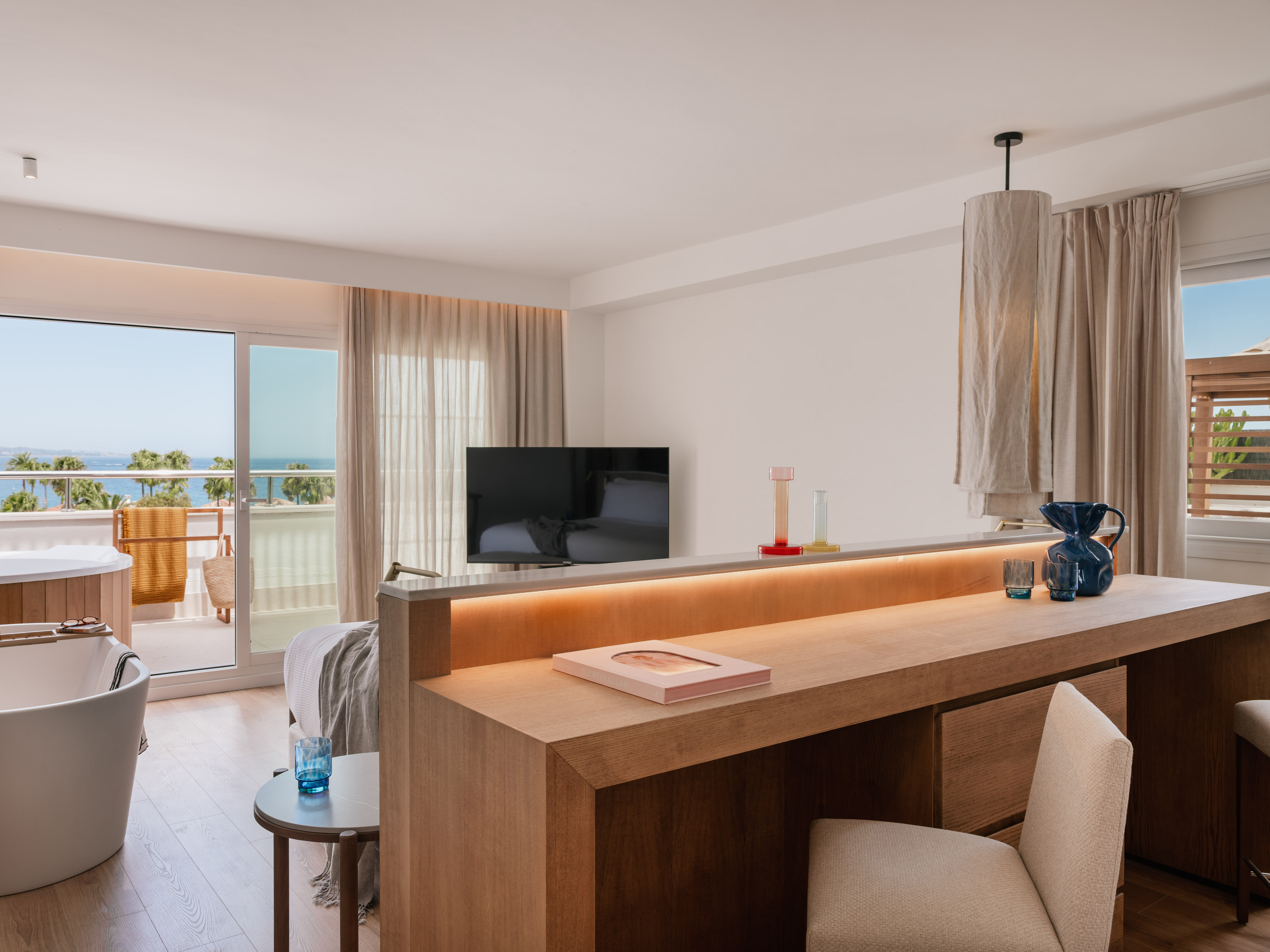 Luxury hotel suite with ocean view balcony, freestanding tub, and wooden bar.