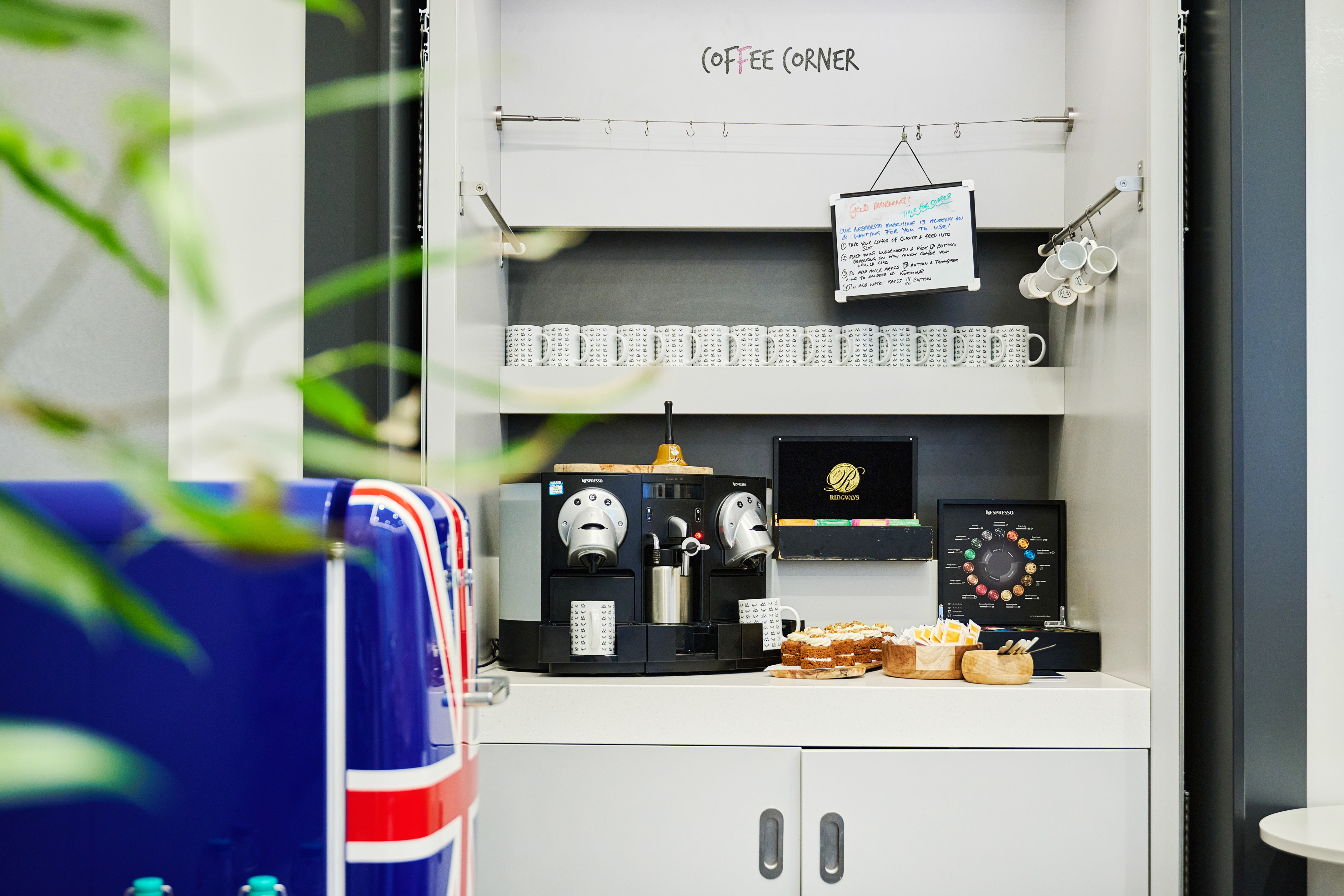 Coffee corner with Nespresso machines, mugs, pastries, and Union Jack appliance.