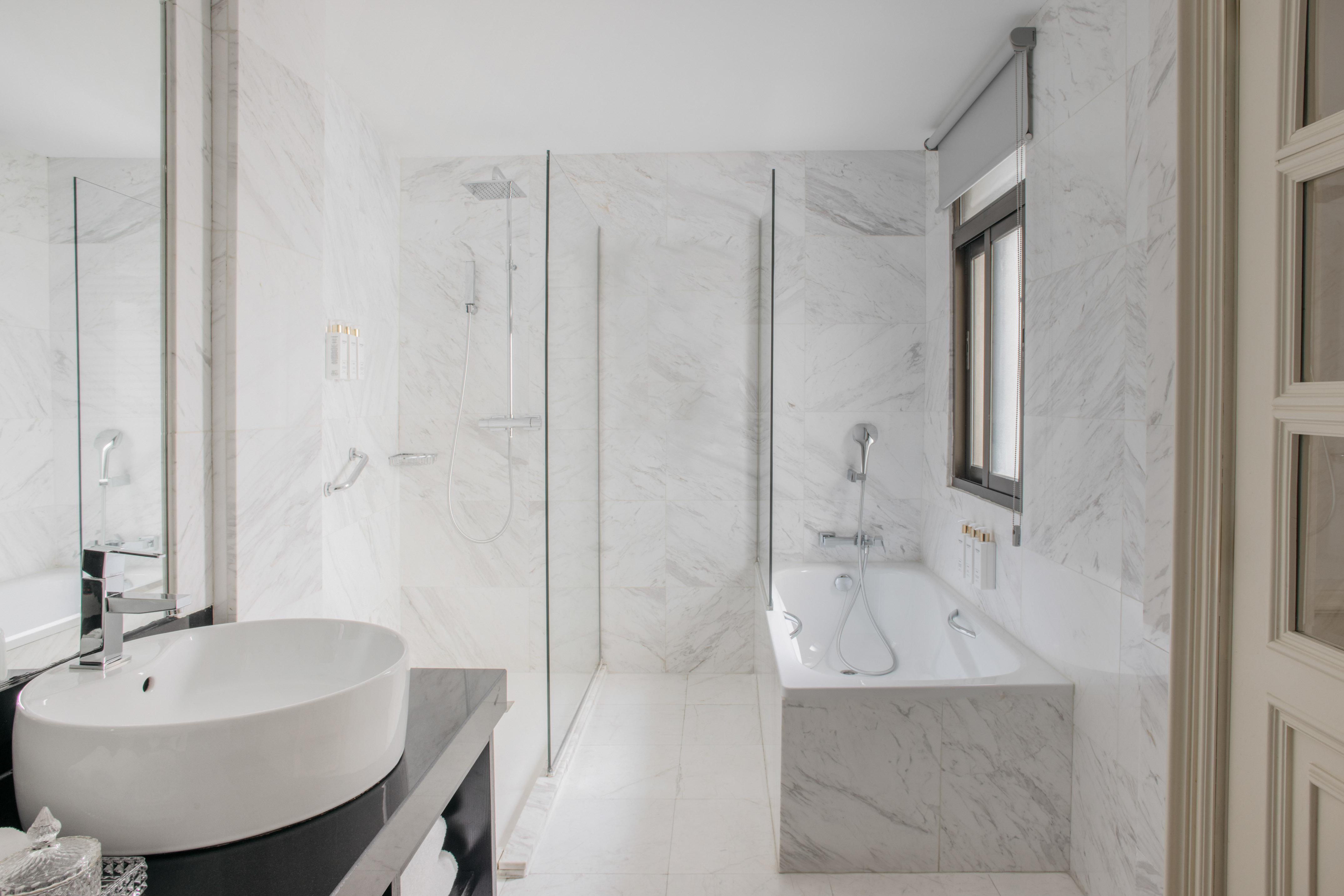 White marble bathroom with walk-in shower, bathtub, and modern vanity sink.
