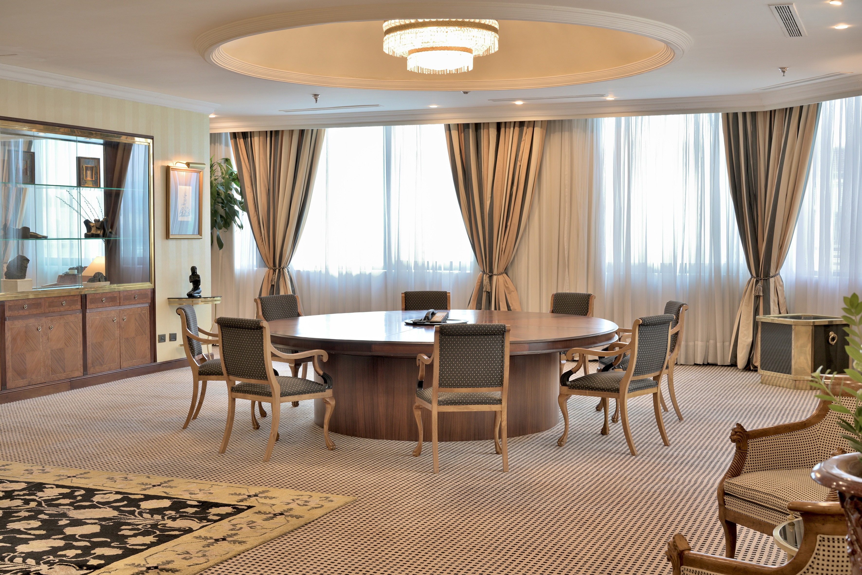 Elegant meeting room with round wooden table, patterned carpet, and large windows.