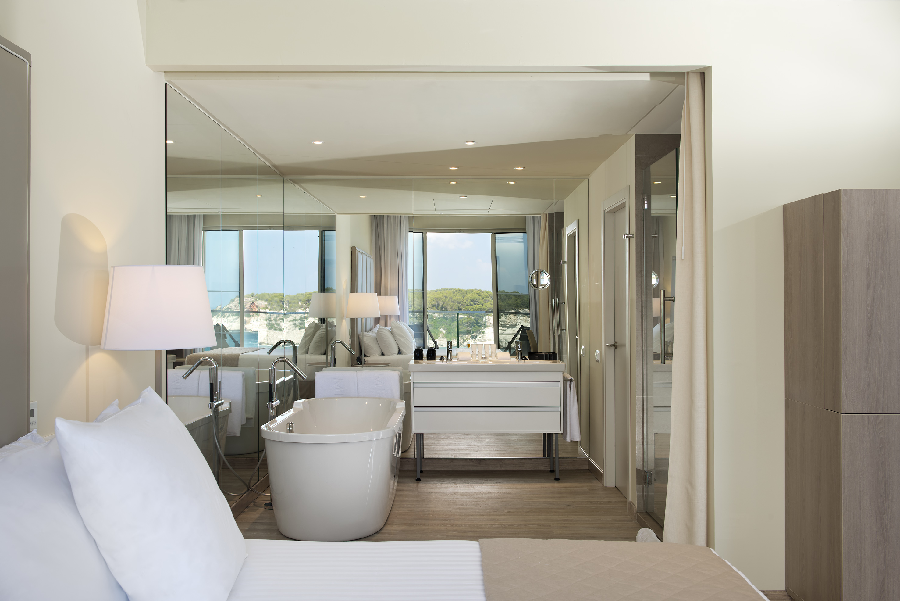 Luxury hotel suite with bed, freestanding bathtub, and ocean view.