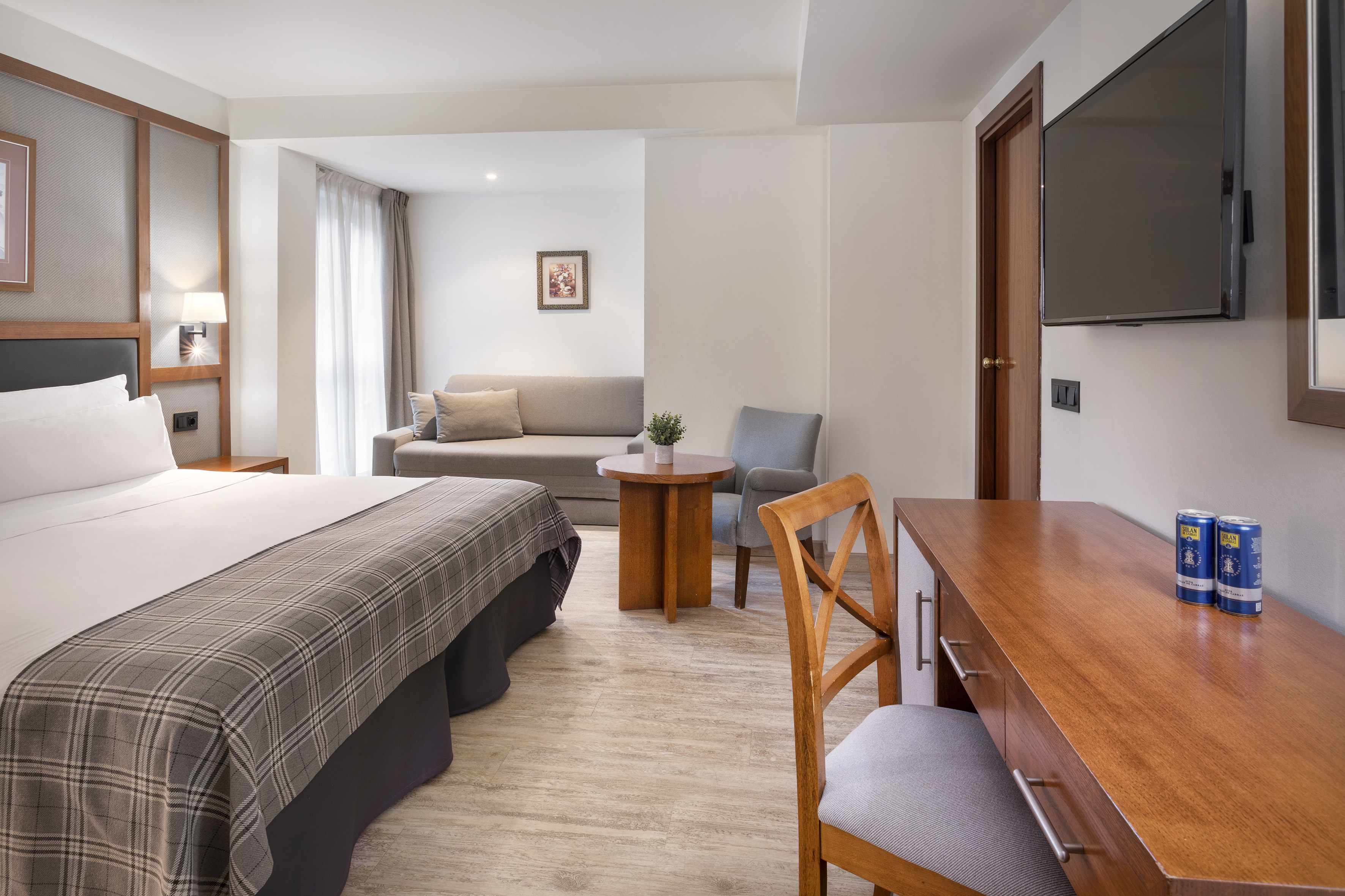 Modern hotel suite with bed, sofa lounge, work desk, and wall TV.