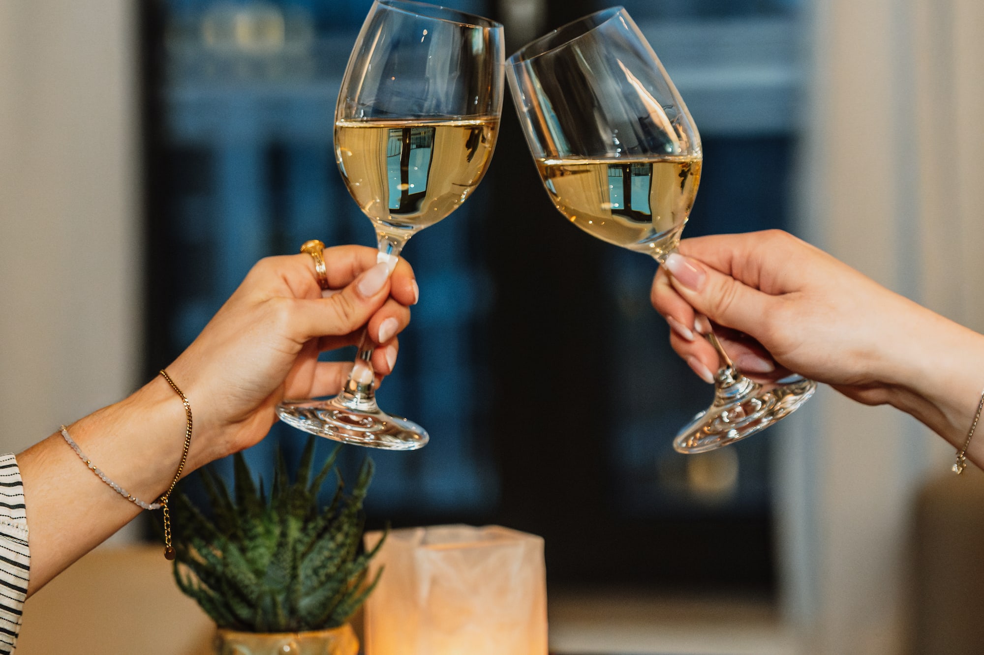 Hands clinking white wine glasses, romantic dinner celebration.