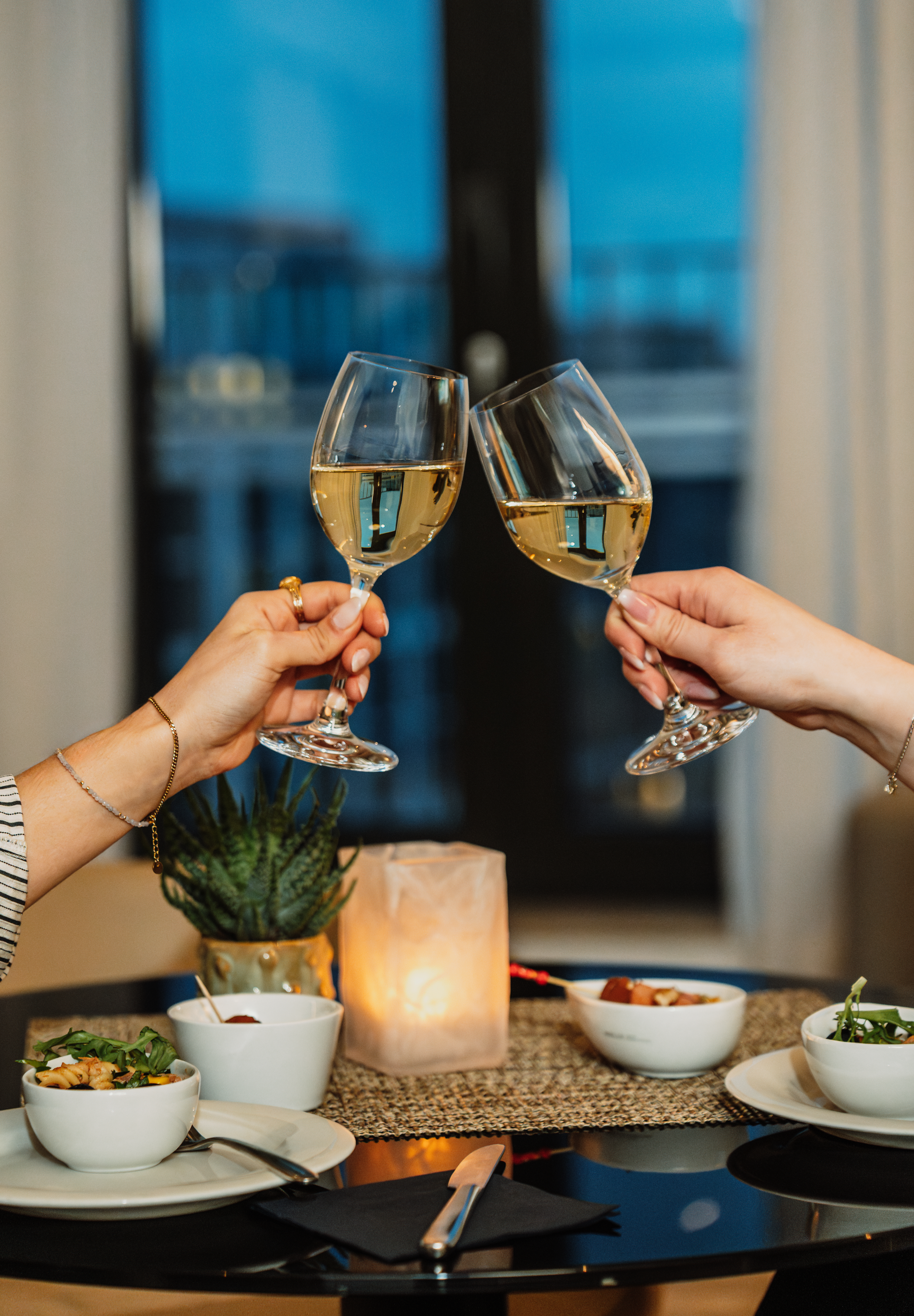 Hands clinking white wine glasses, romantic dinner celebration.