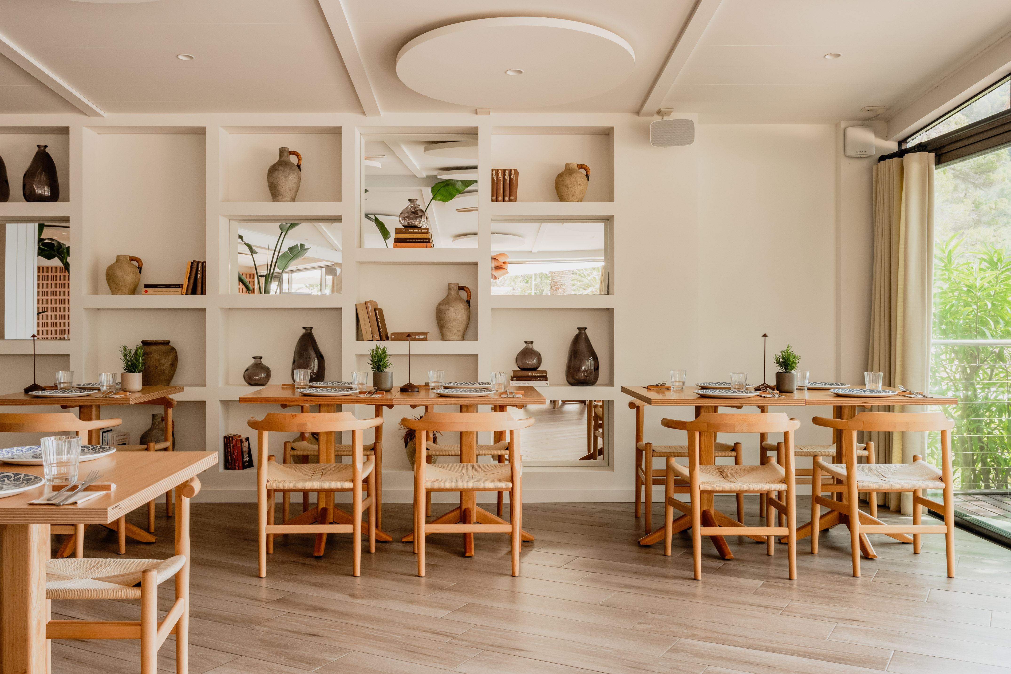 Bright restaurant interior with wood tables, woven chairs, and styled shelves.