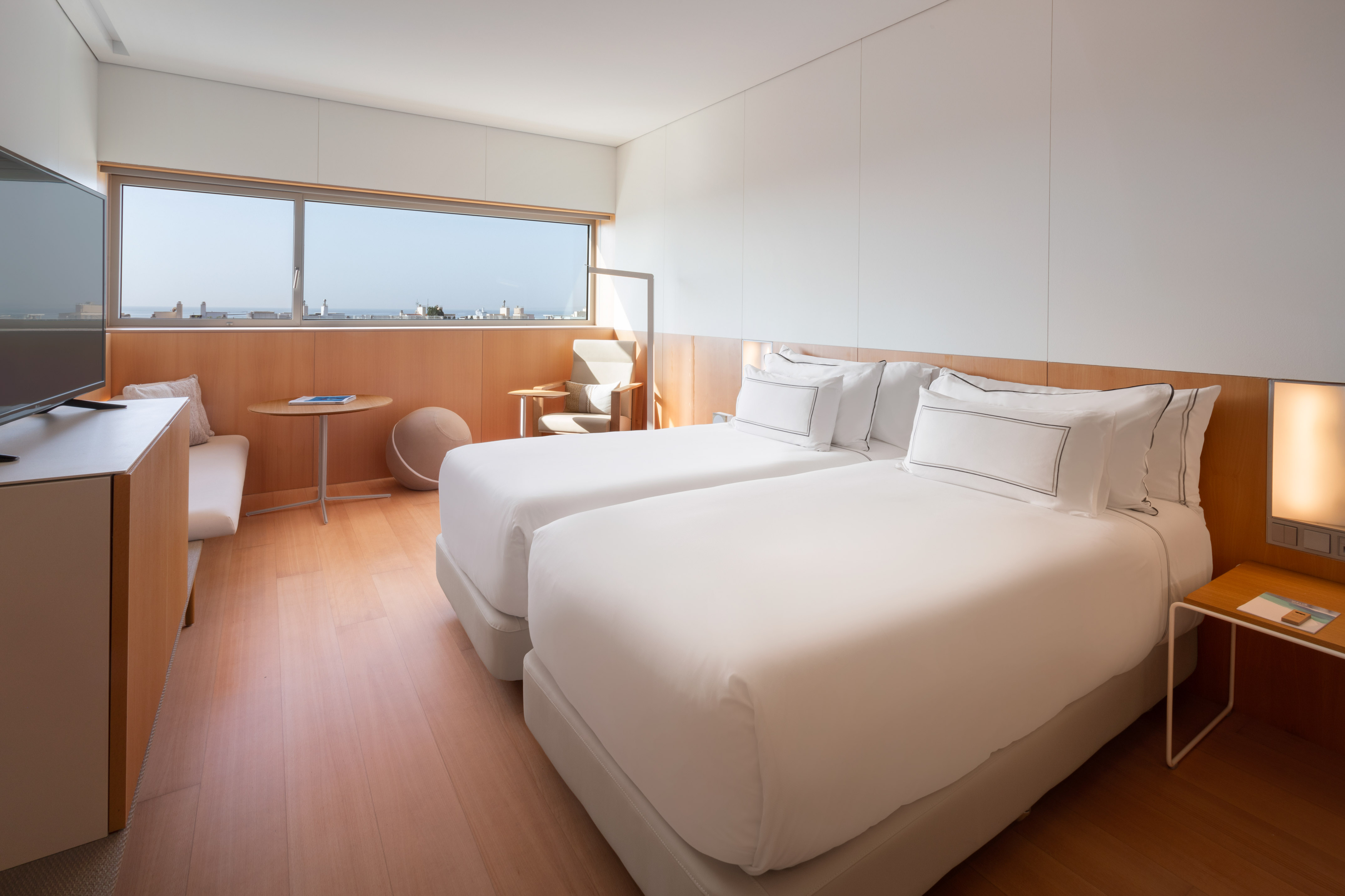 Modern hotel room with twin beds, wood furniture, and window city/sea view.