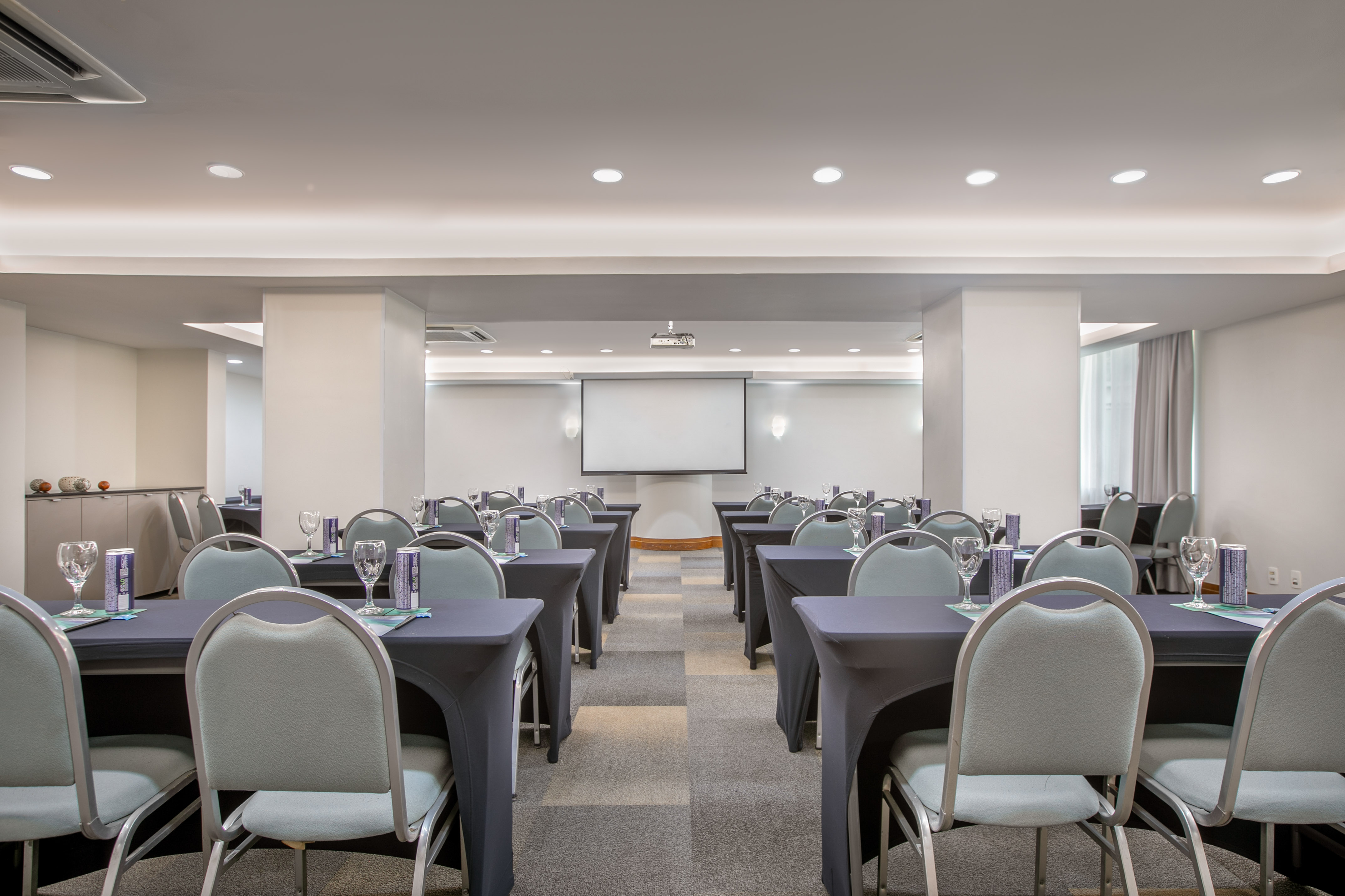 Empty conference room with tables, chairs, and projector screen for meetings.