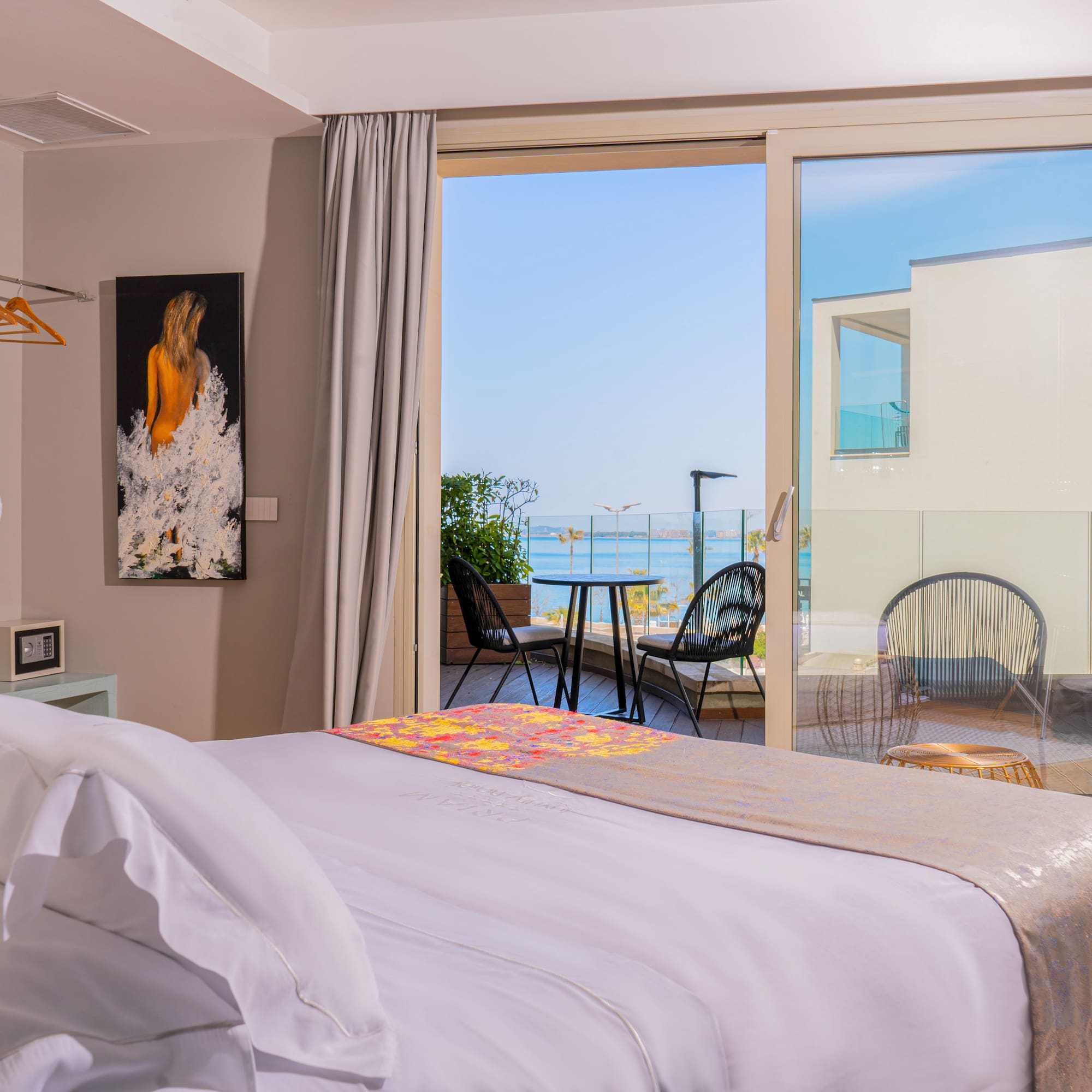 Bright hotel room with sea view balcony, white bed, and outdoor seating.
