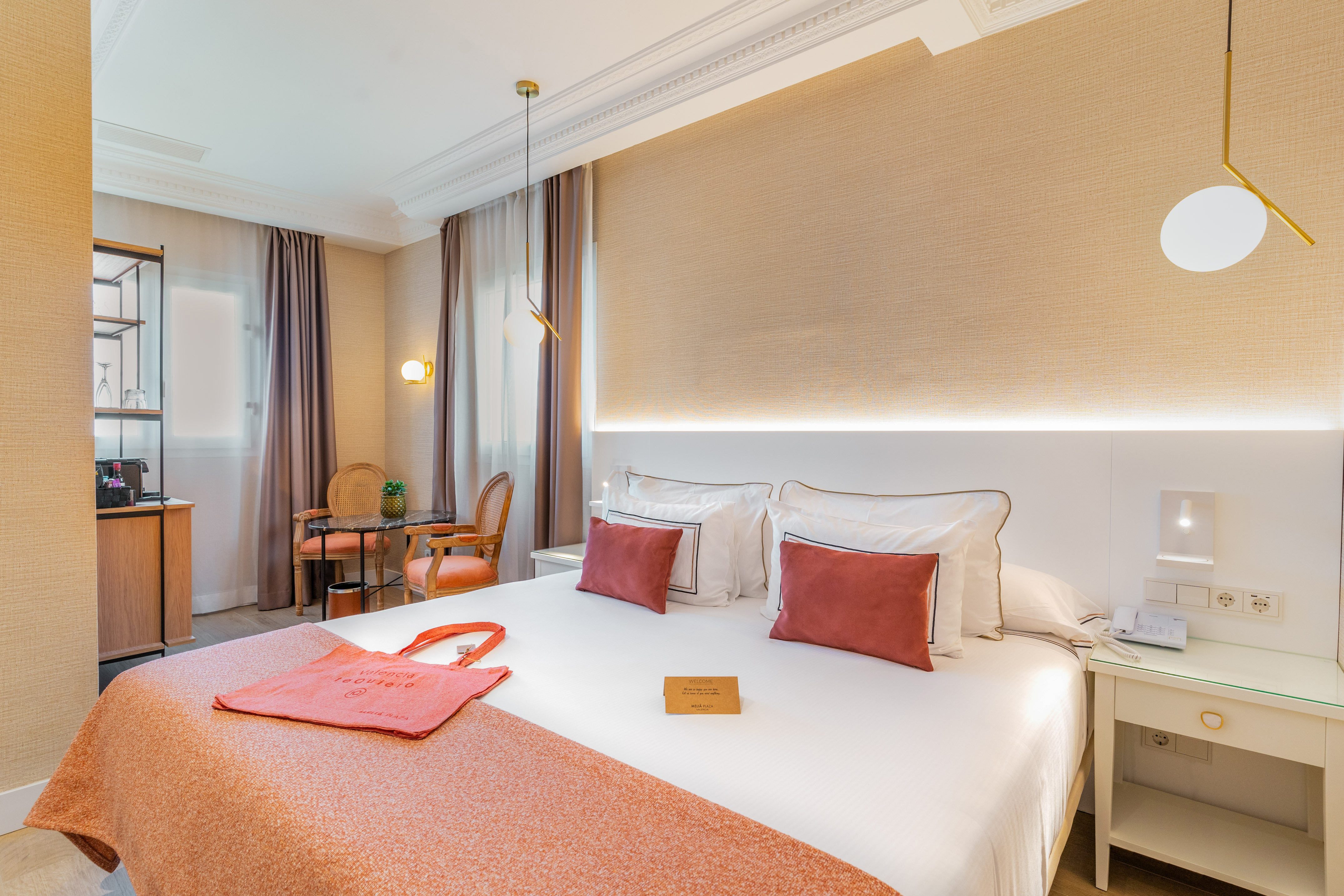 Modern hotel room with a large bed, coral accents, and a comfortable seating area.
