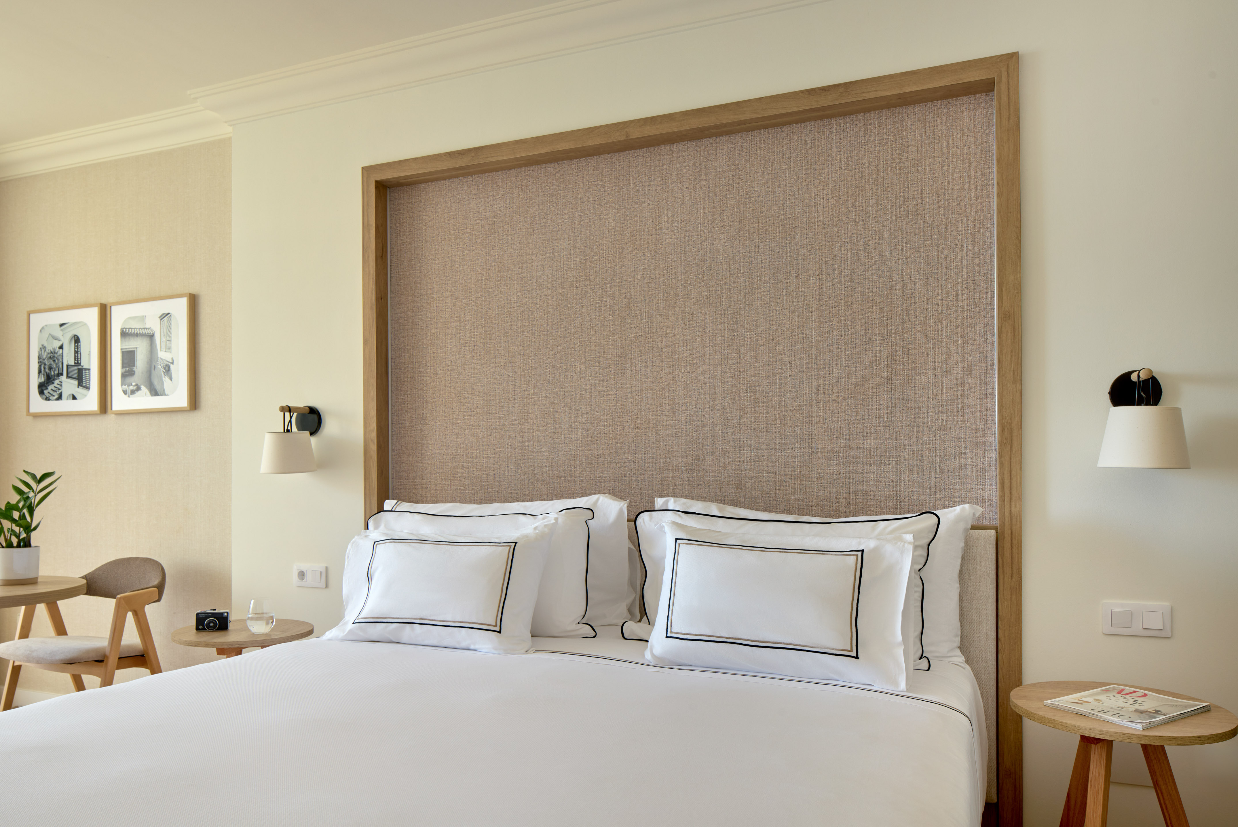 Modern hotel bedroom with white bed, wooden headboard, and bedside furniture.