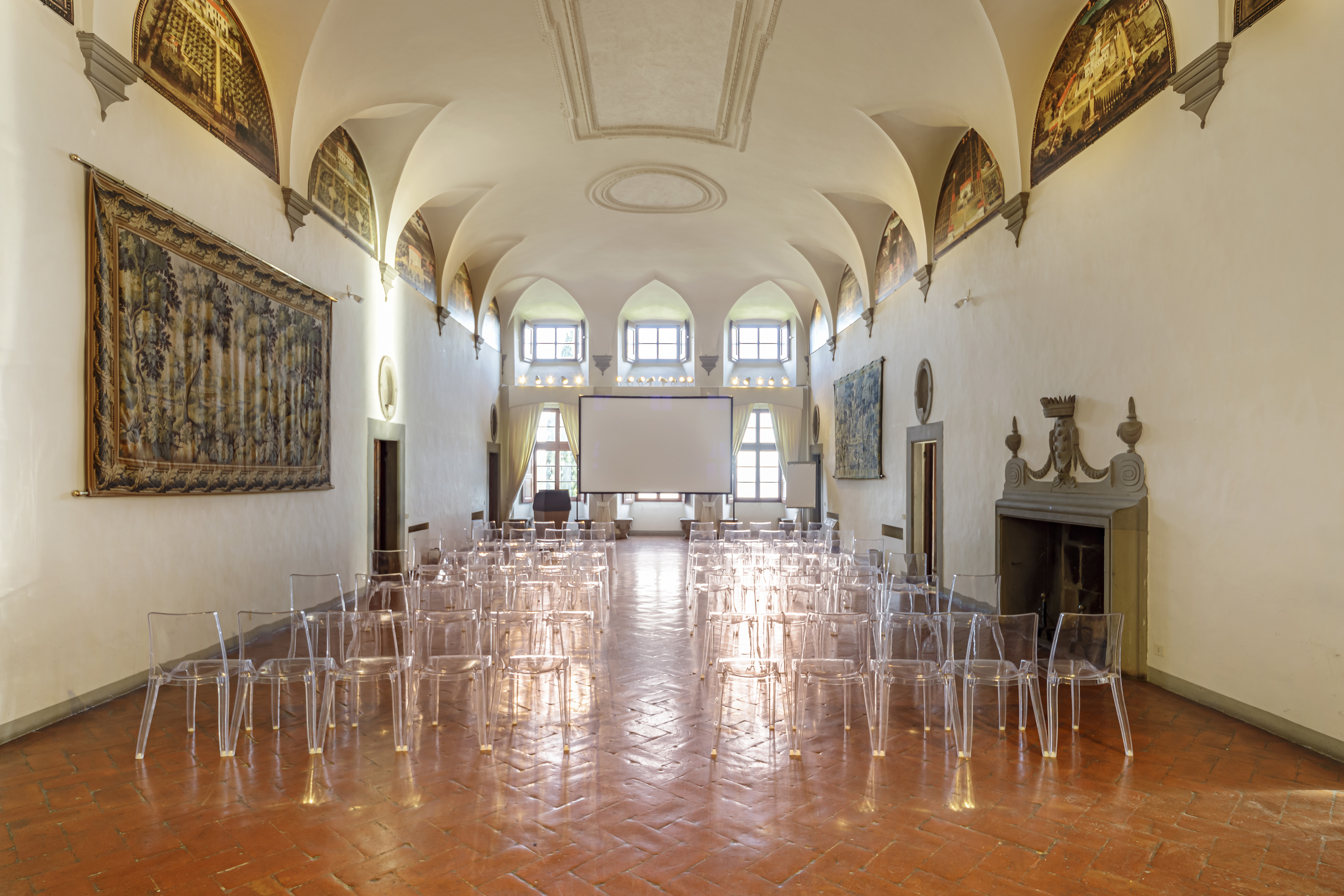 Vaulted historic event room with clear chairs, projection screen, and frescoes.