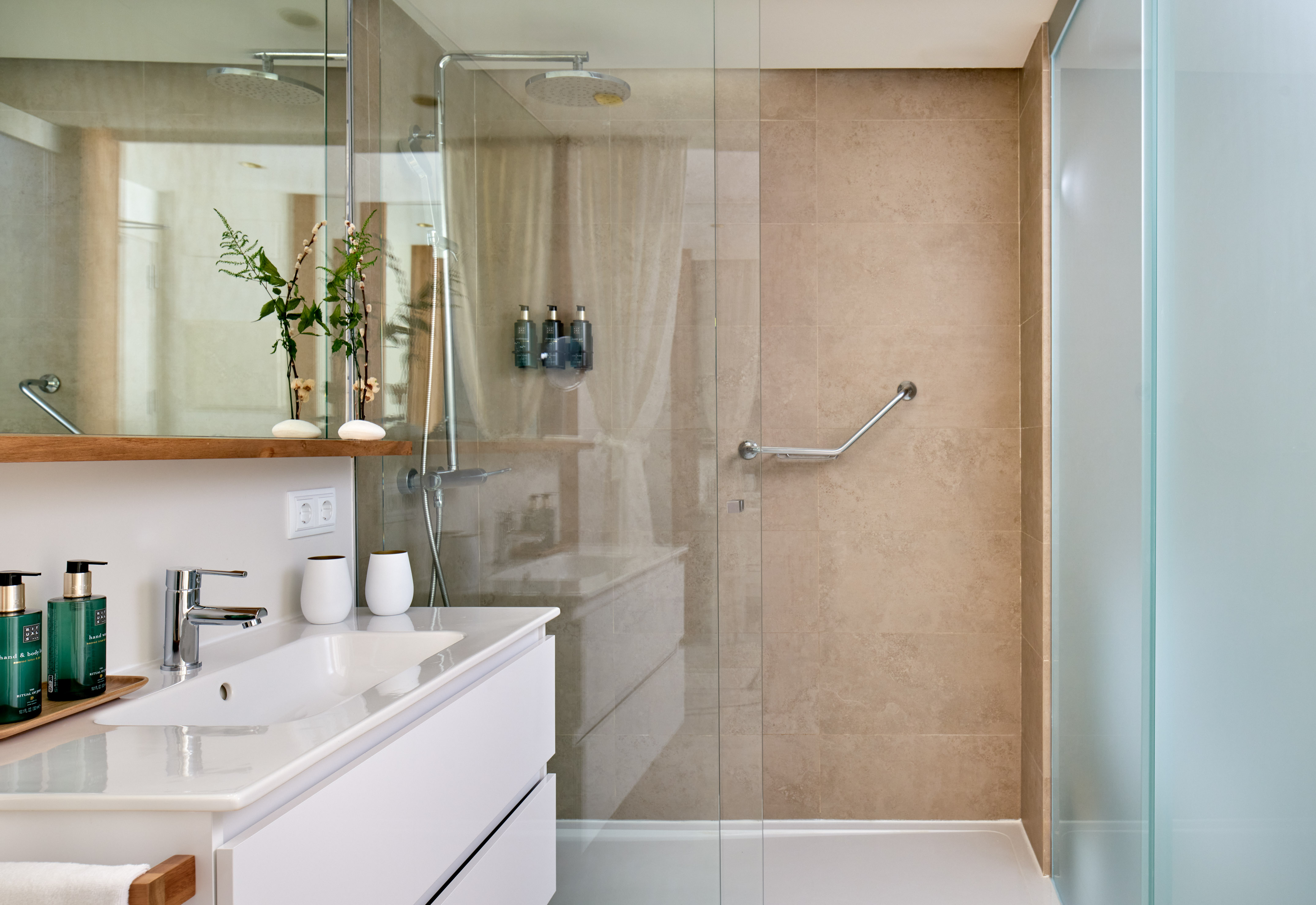 Modern bathroom with glass shower, grab bar, vanity, and beige tiles.