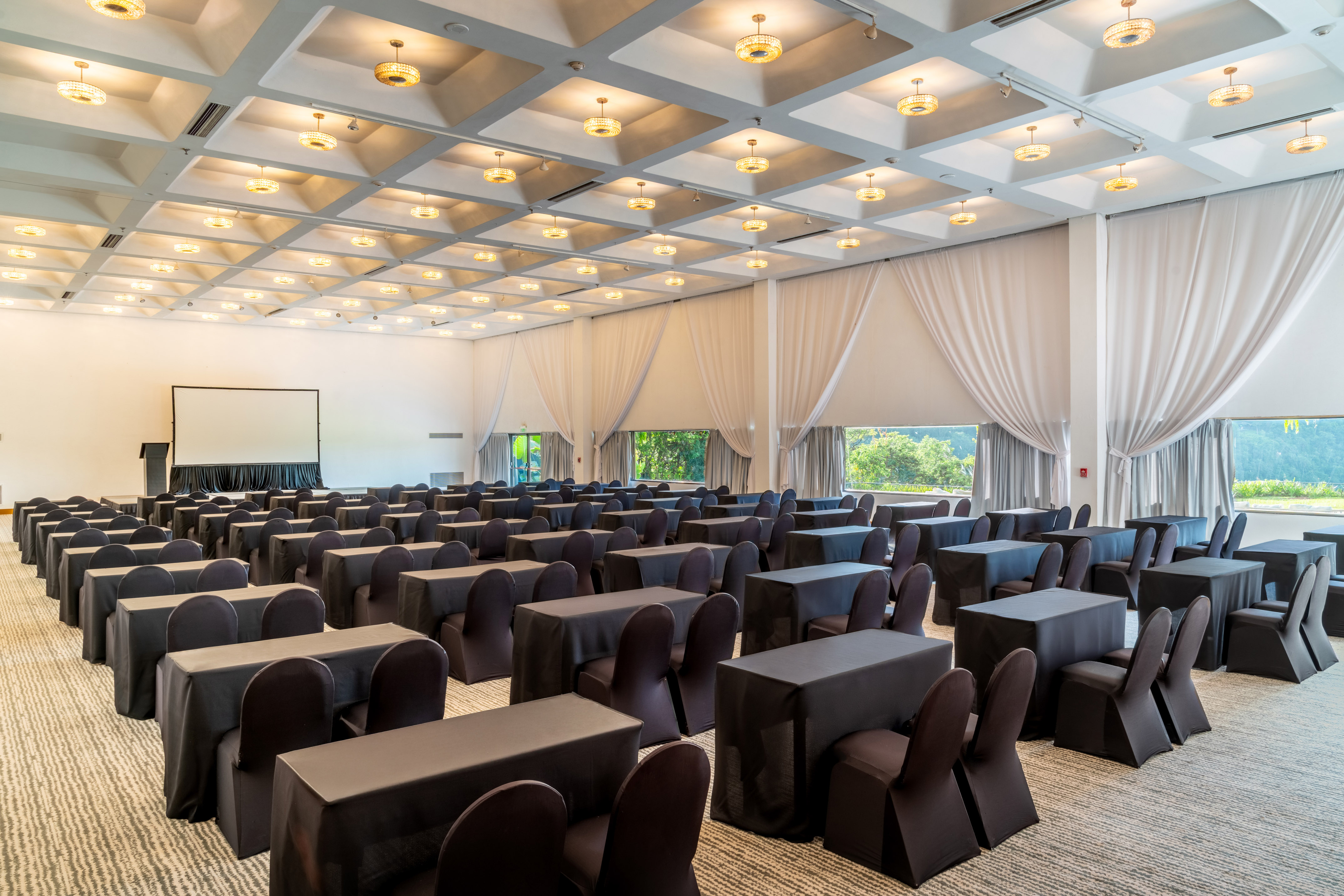 Modern event space with black tables, chairs, projector, and window views.