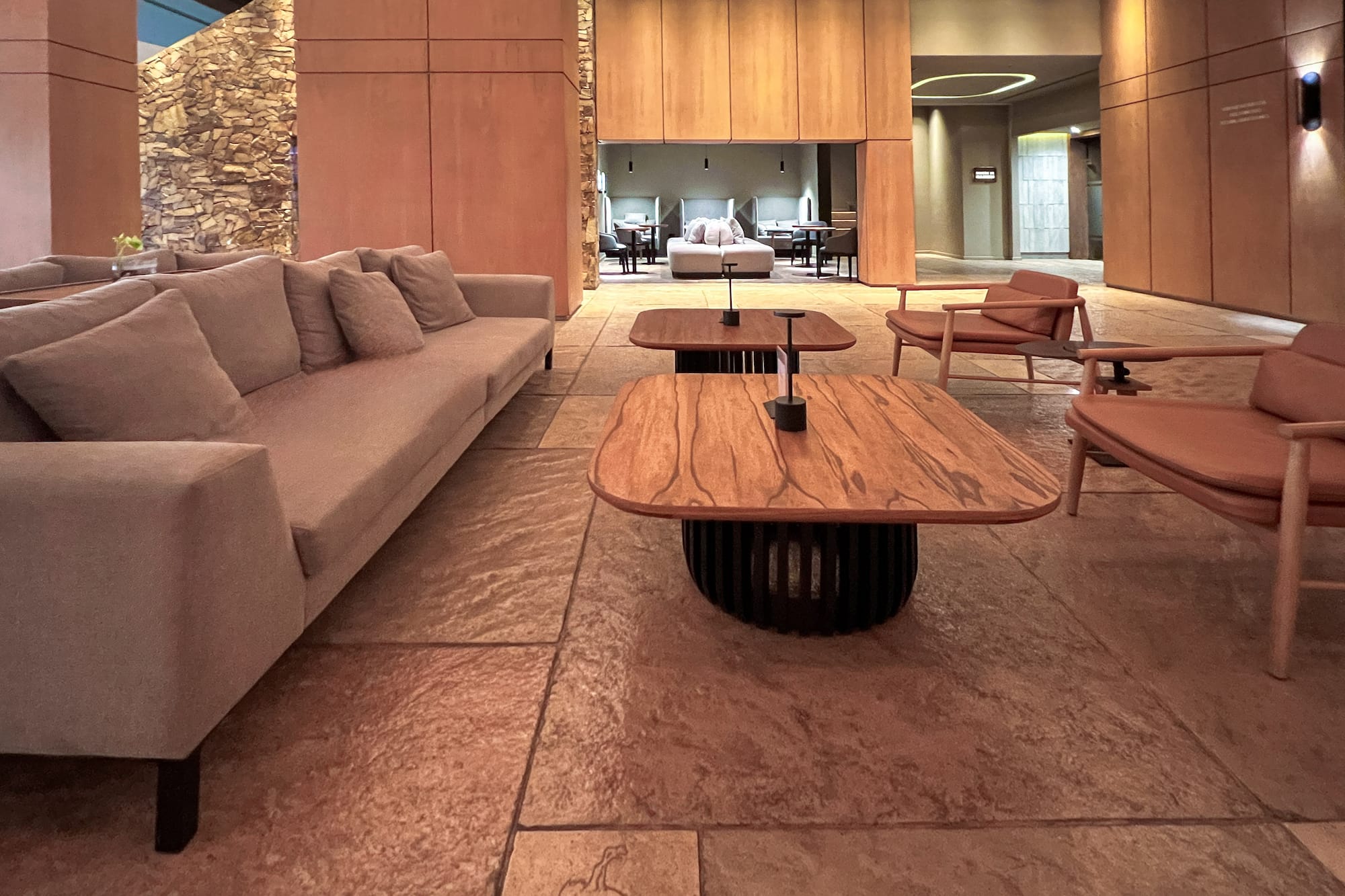 Modern hotel lounge with wood panels, stone wall, sofa, and lounge chairs.