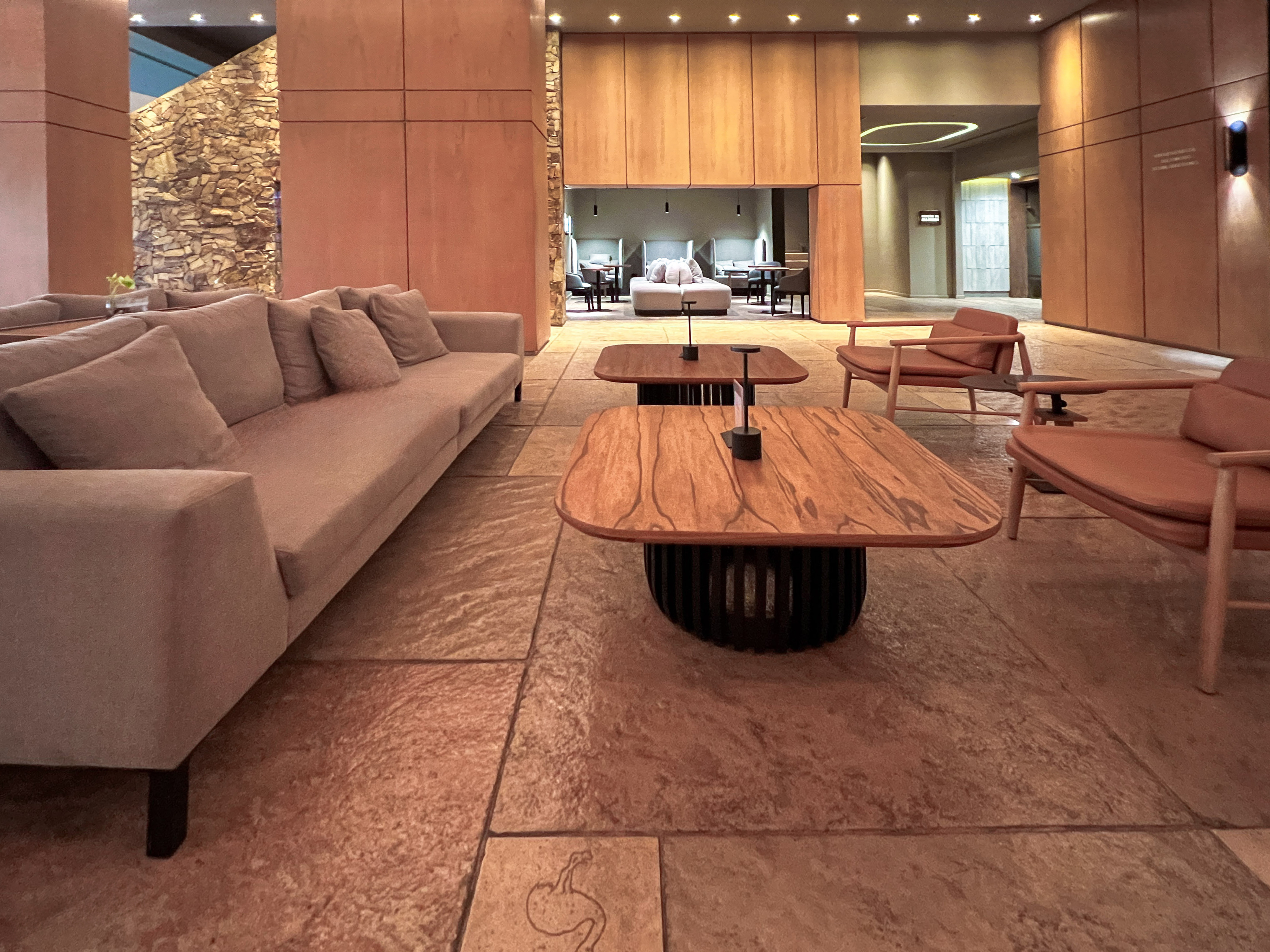 Modern hotel lounge with wood panels, stone wall, sofa, and lounge chairs.