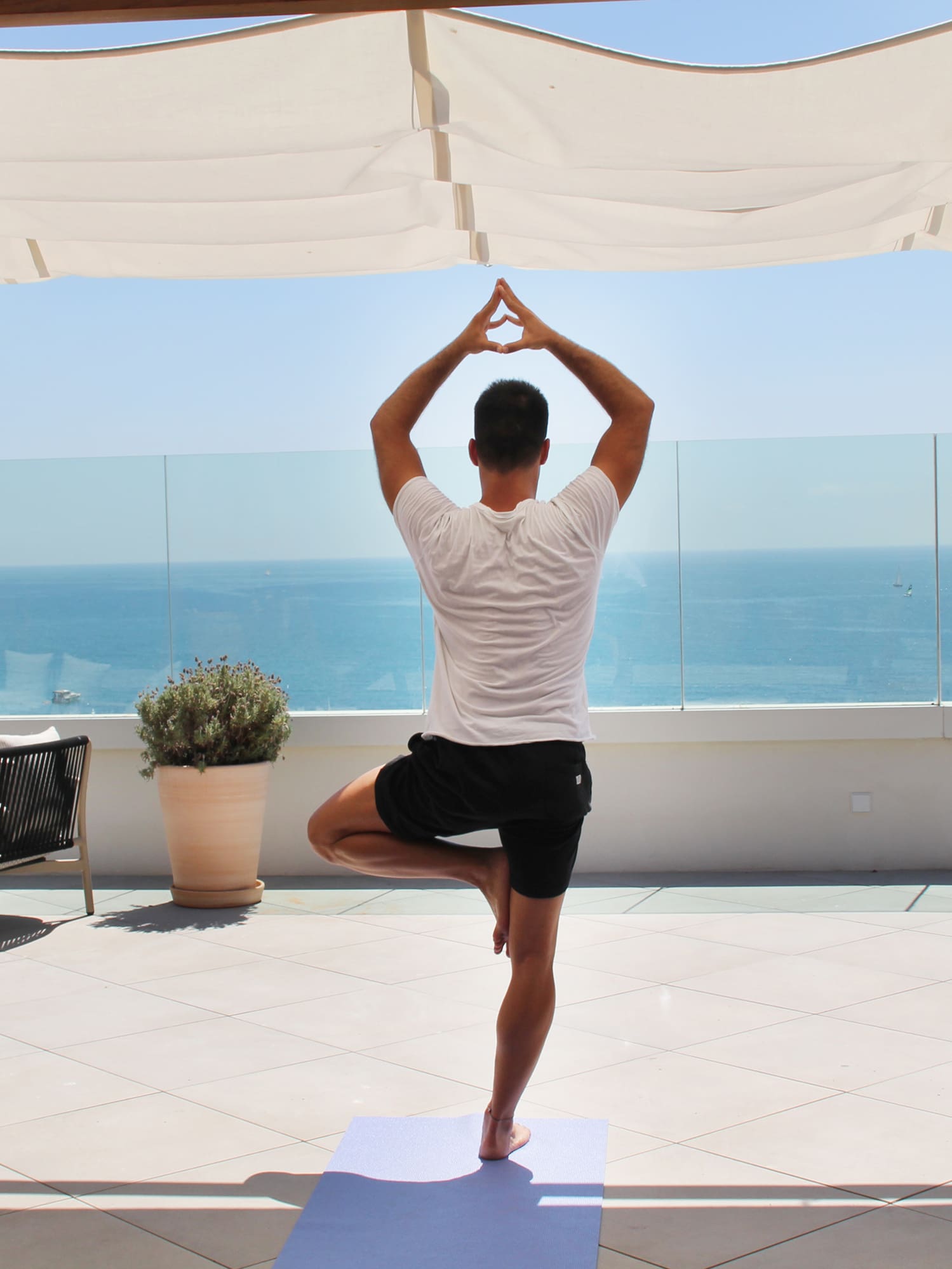 a man standing on one leg on a yoga mat with a body of water in the background