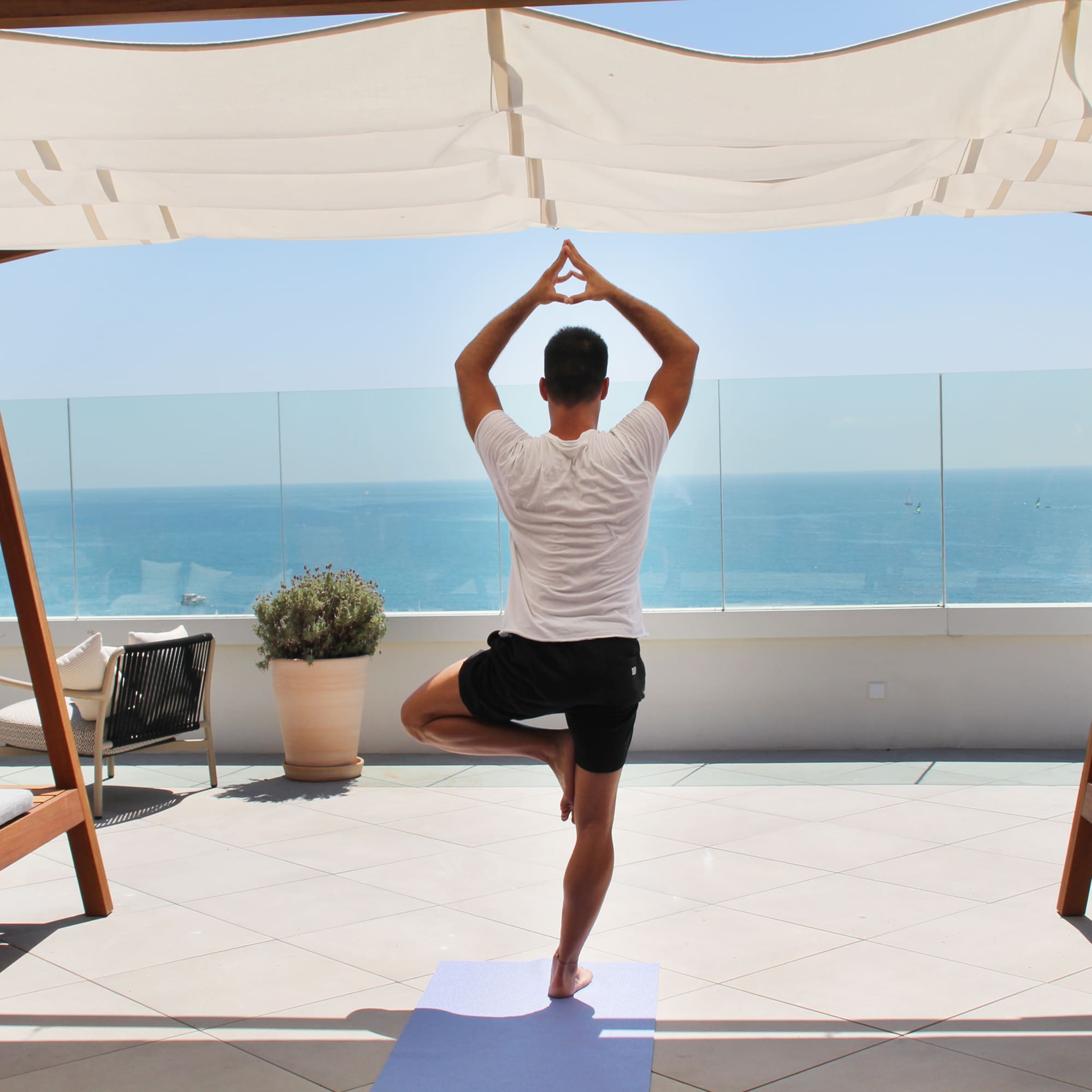 a man standing on one leg on a yoga mat with a body of water in the background