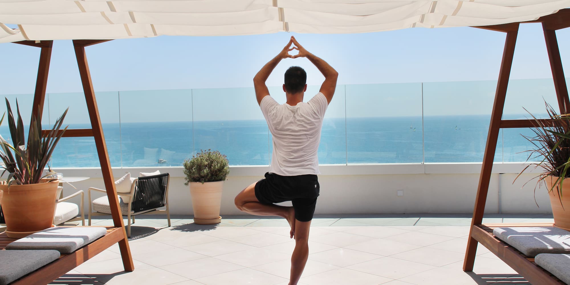 a man standing on one leg on a yoga mat with a body of water in the background