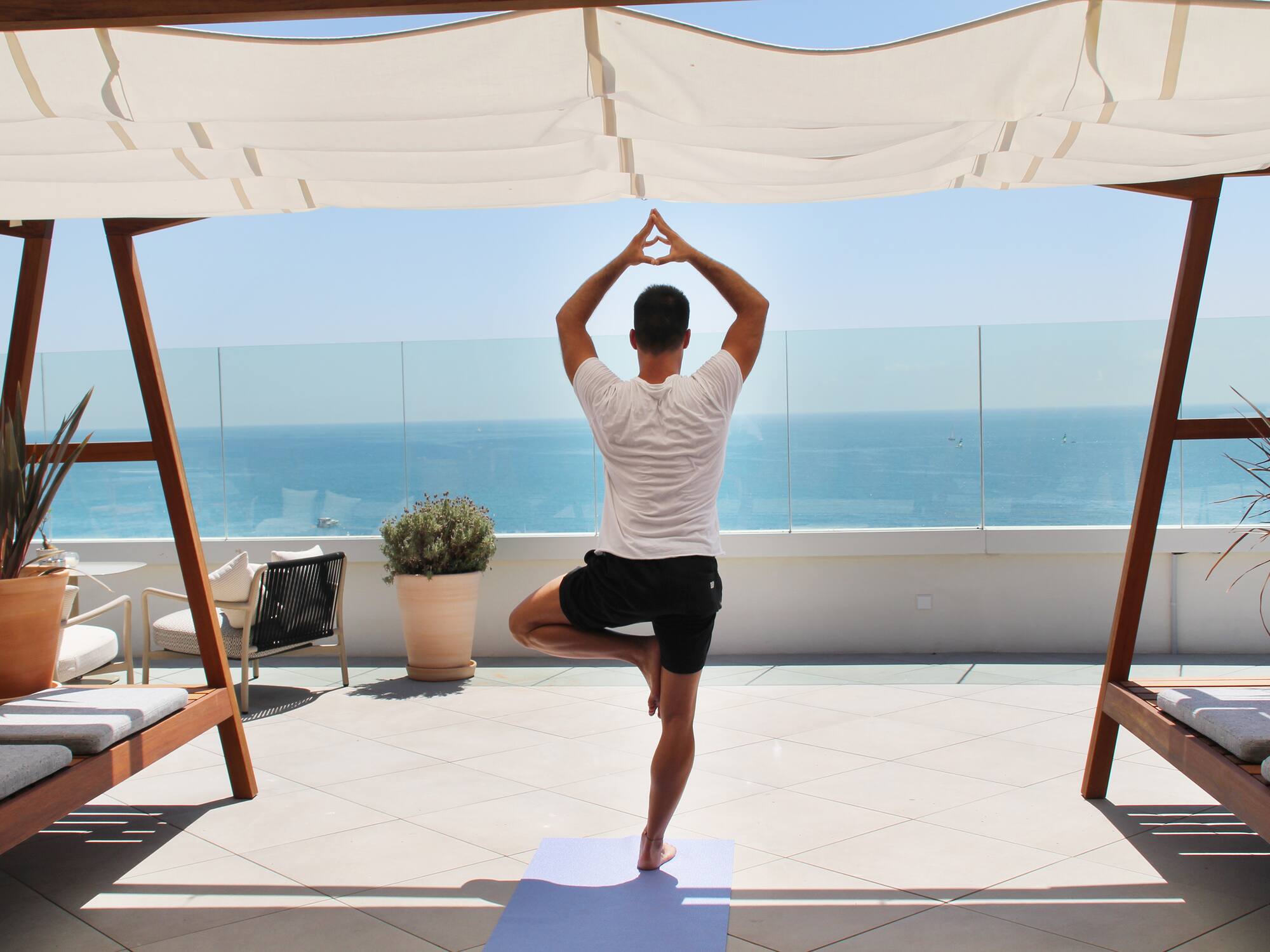 a man standing on one leg on a yoga mat with a body of water in the background
