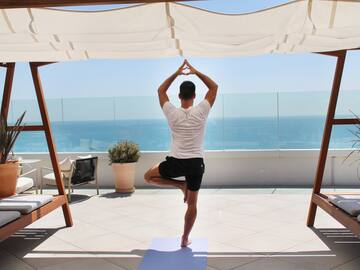 a man standing on one leg on a yoga mat with a body of water in the background