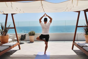 a man standing on one leg on a yoga mat with a body of water in the background