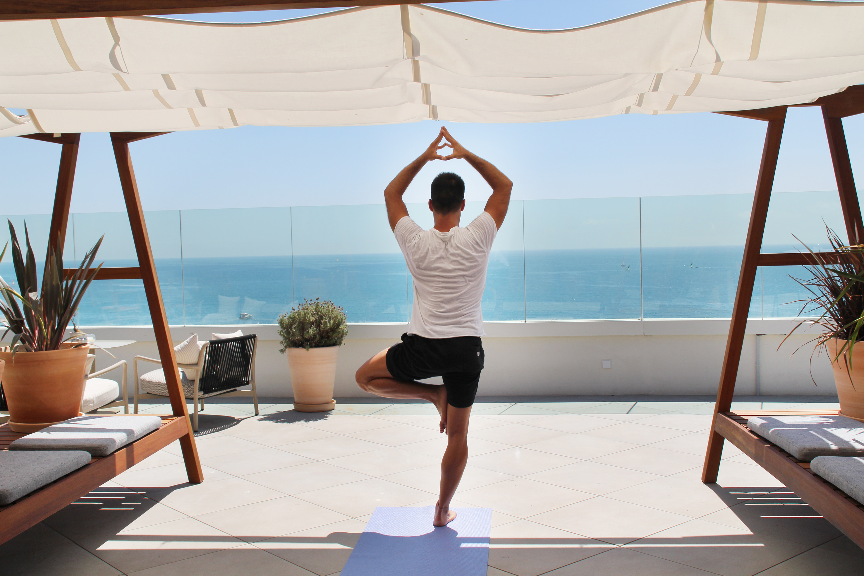 Man in Tree Pose yoga on a patio overlooking the blue ocean.