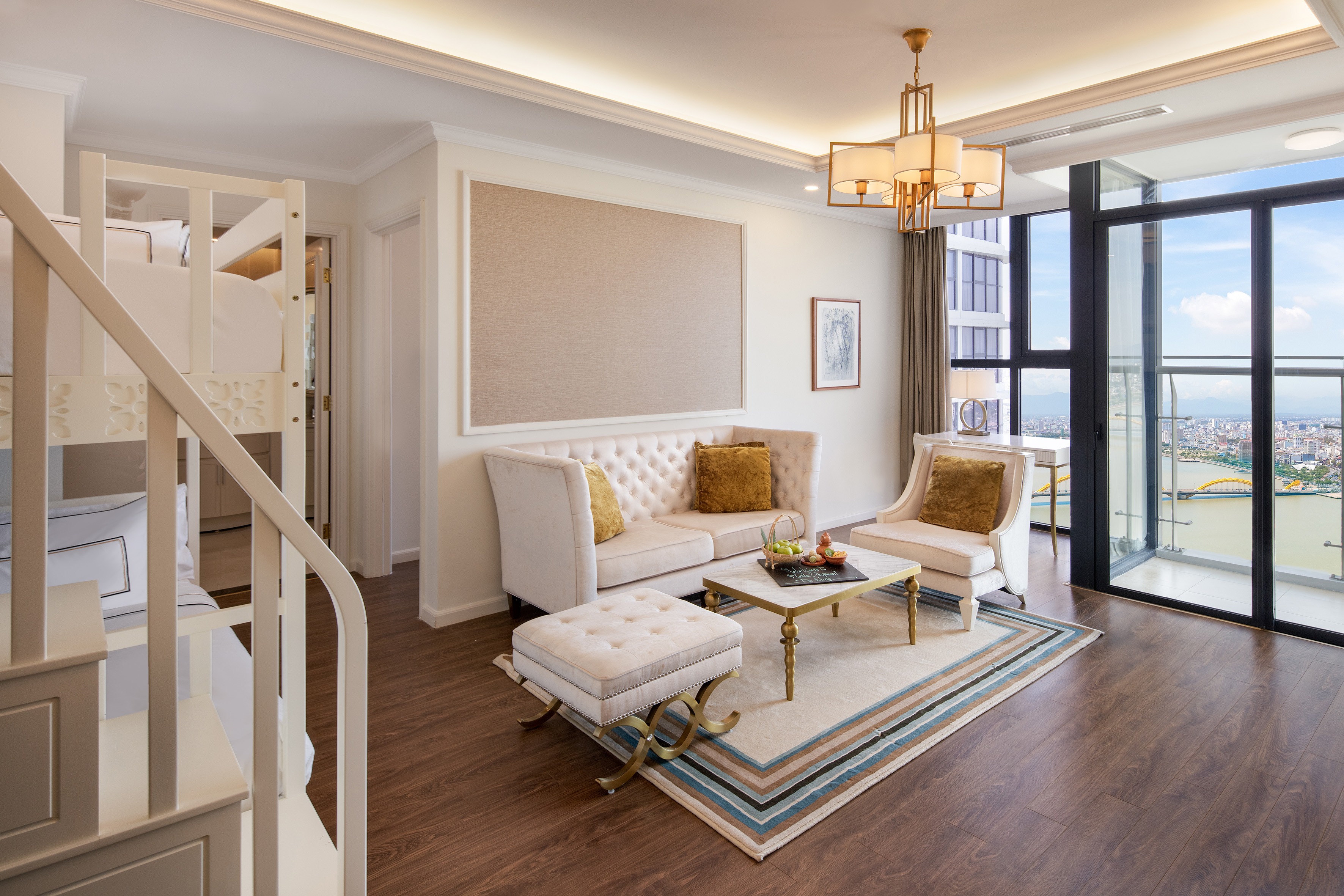 Modern hotel suite living room with sofa, bunk beds, and city view.