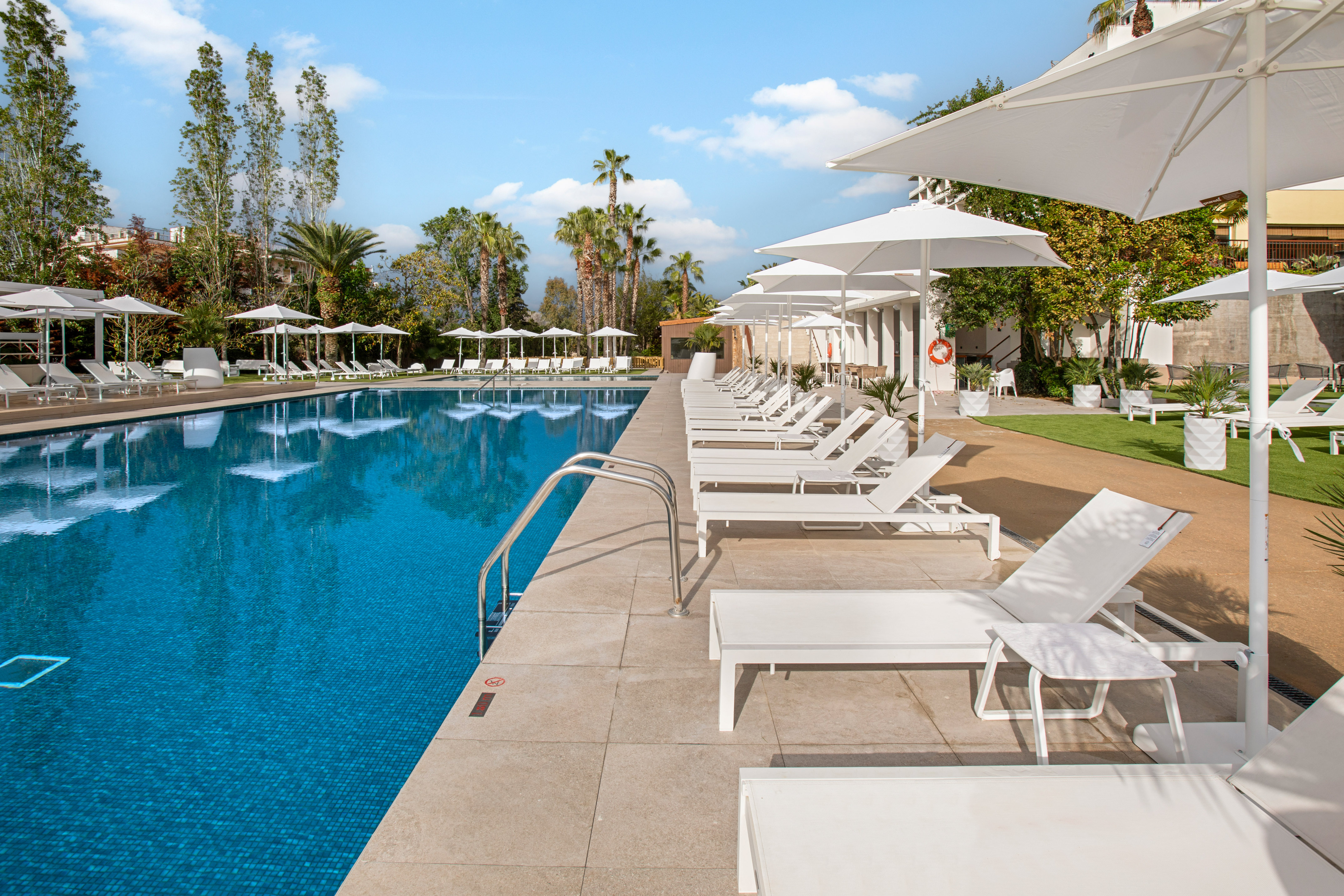 Luxury resort pool with white lounge chairs, umbrellas, and palm trees.